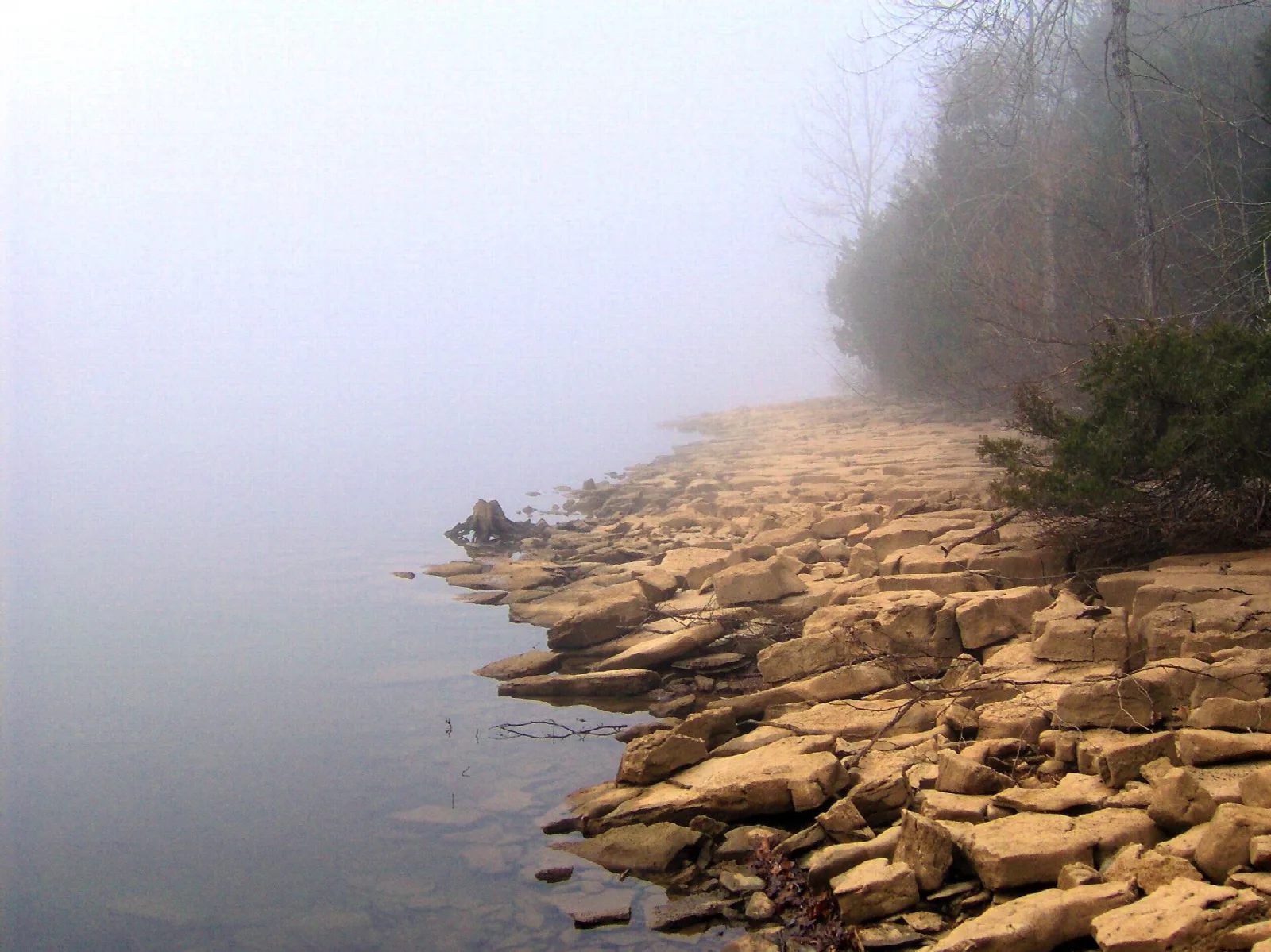 Flat rocky shoreline fading into misty lake water