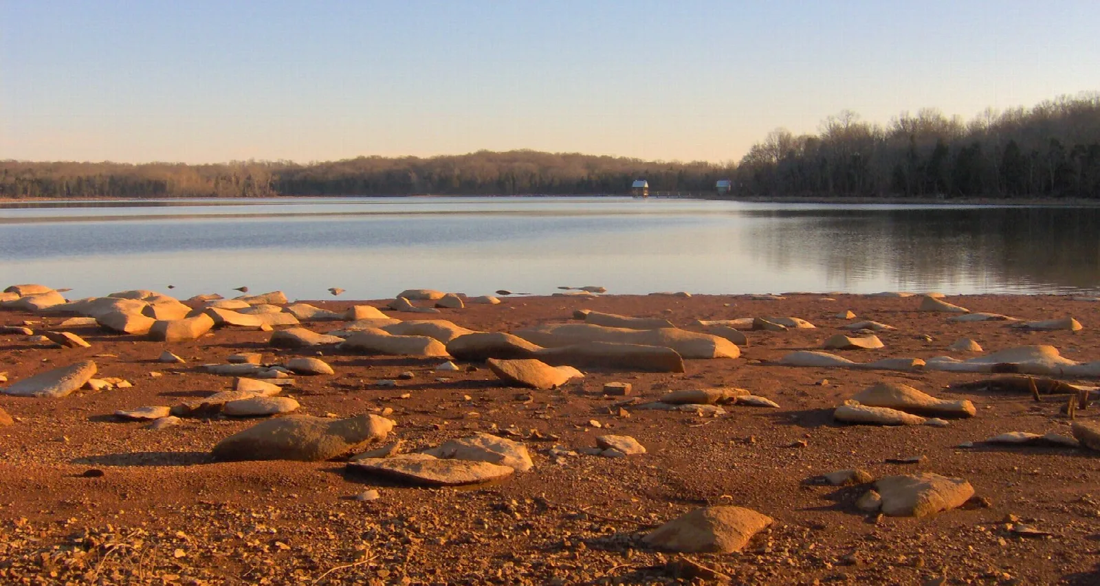 Still lake at dusk with a rocky red-brown beach