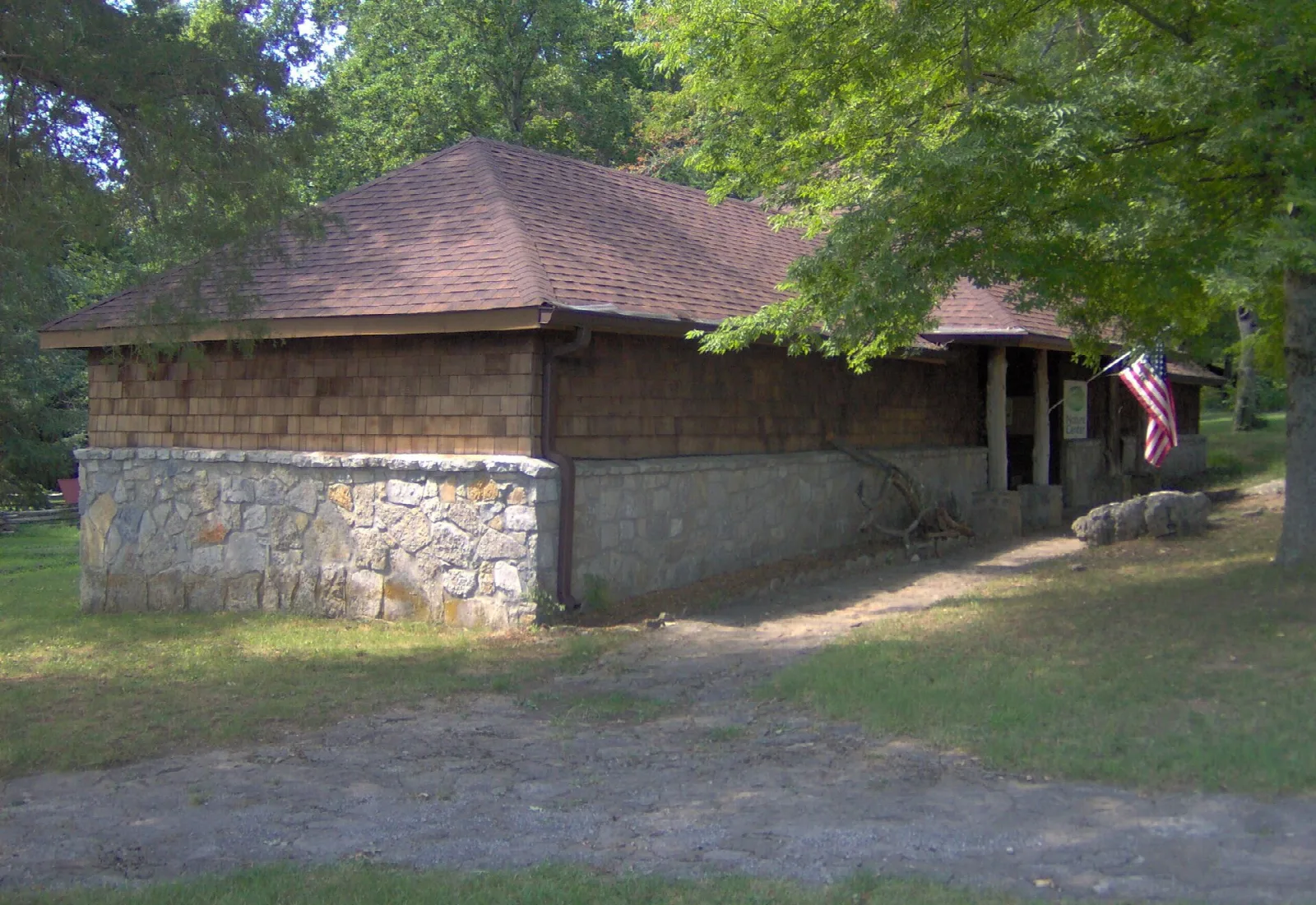 Stone-based building with a shingled roof under trees
