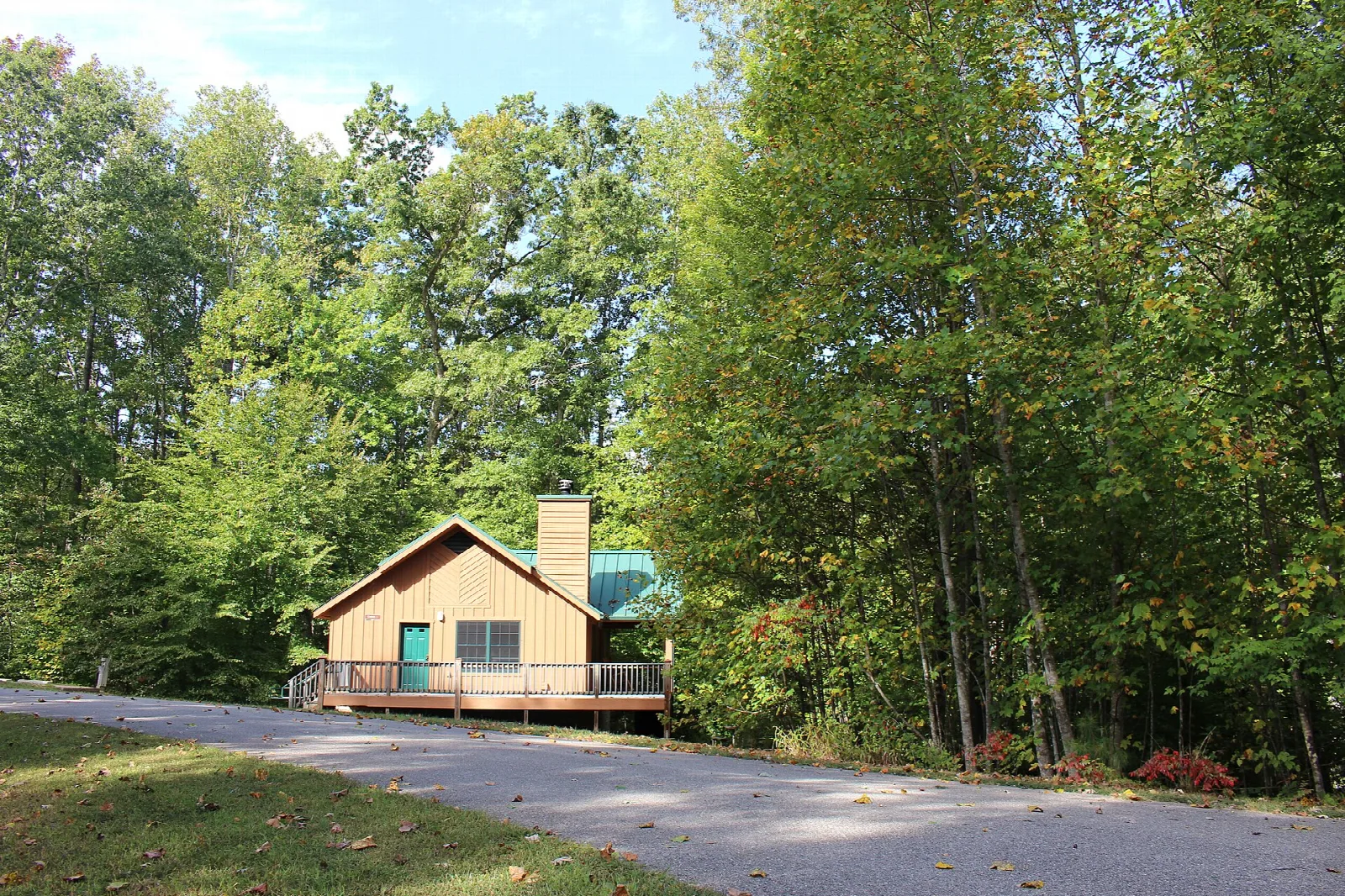 Small cabin beside a paved road surrounded by green trees