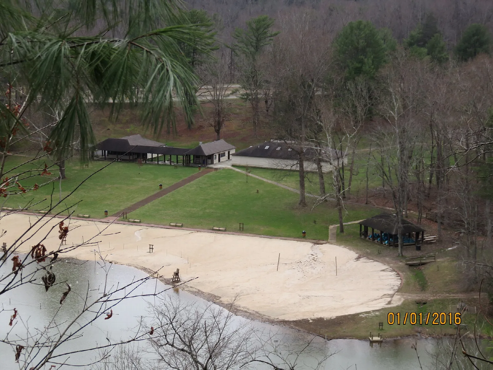 Sandy beach and picnic area beside a lake seen from above, with bare trees