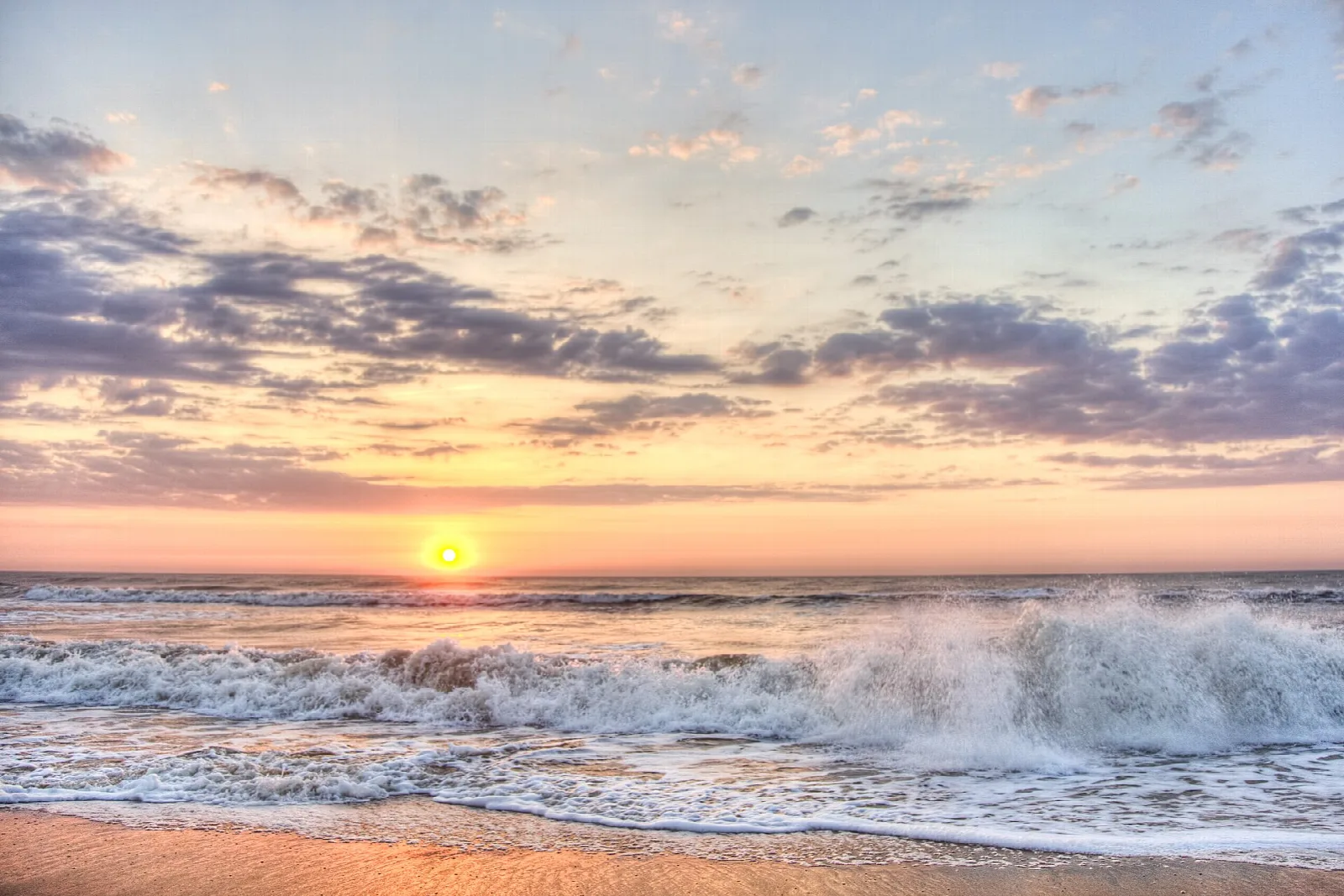 Waves rolling onto a beach under a colorful sunrise sky