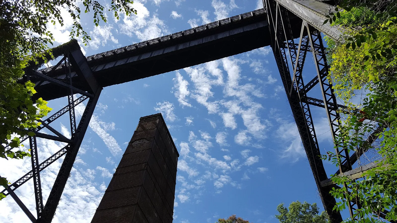 Looking up through bridge ironwork and a brick pier at blue sky