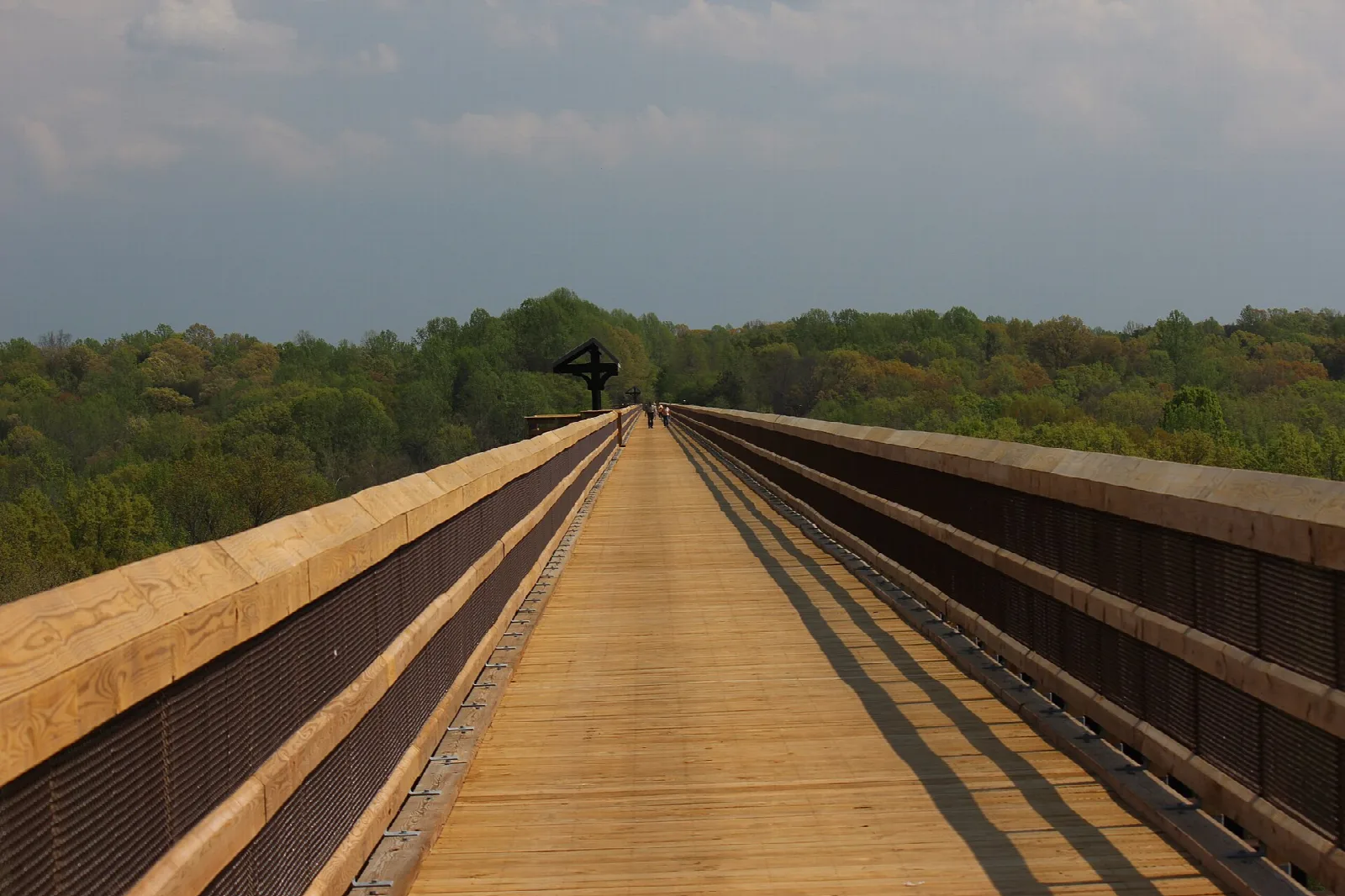 Straight bridge deck with wooden railings running toward the tree line