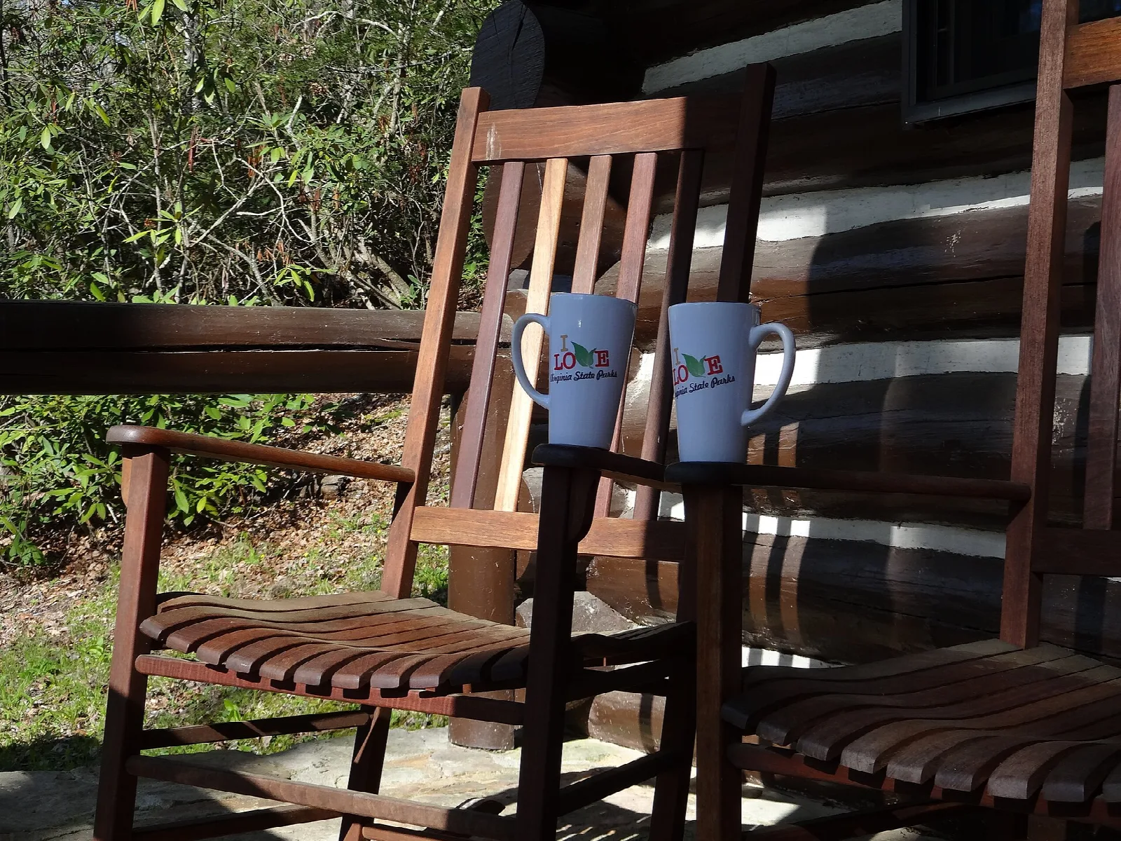 Two rocking chairs with mugs on a log cabin porch