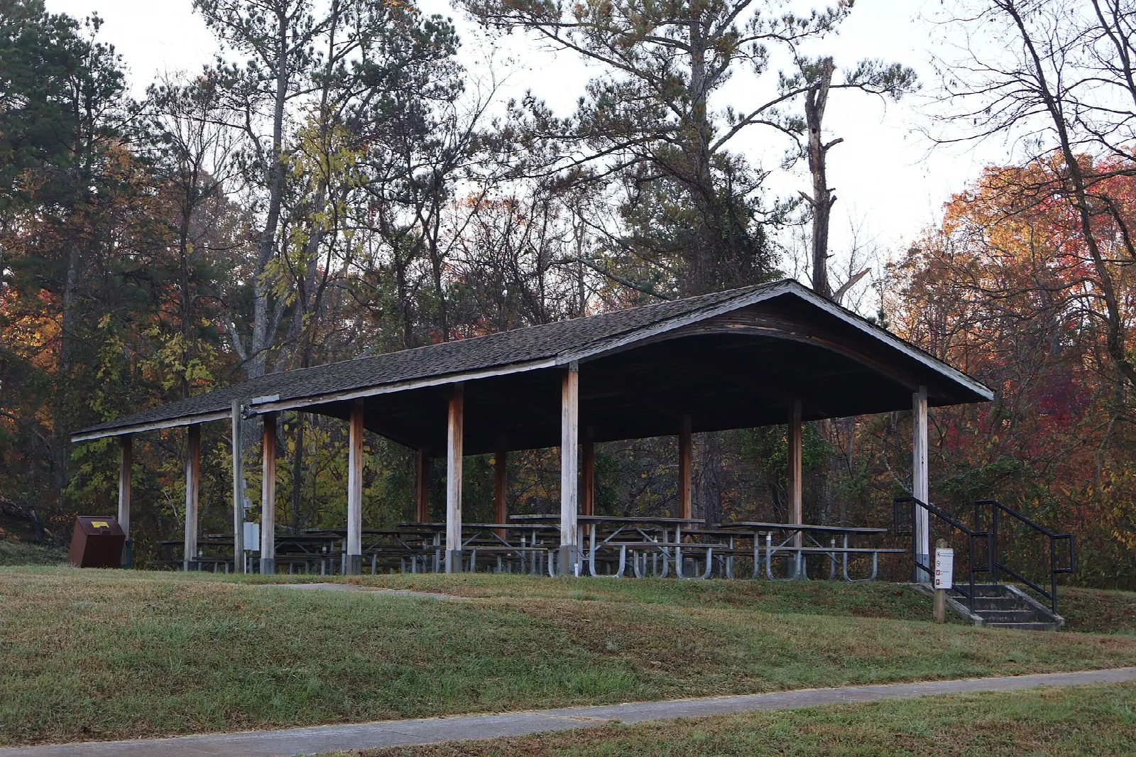 Open-sided picnic shelter on a lawn with autumn trees behind