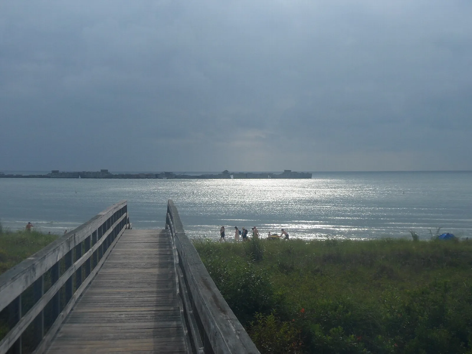 Wooden walkway through dune grass to the bay under gray skies