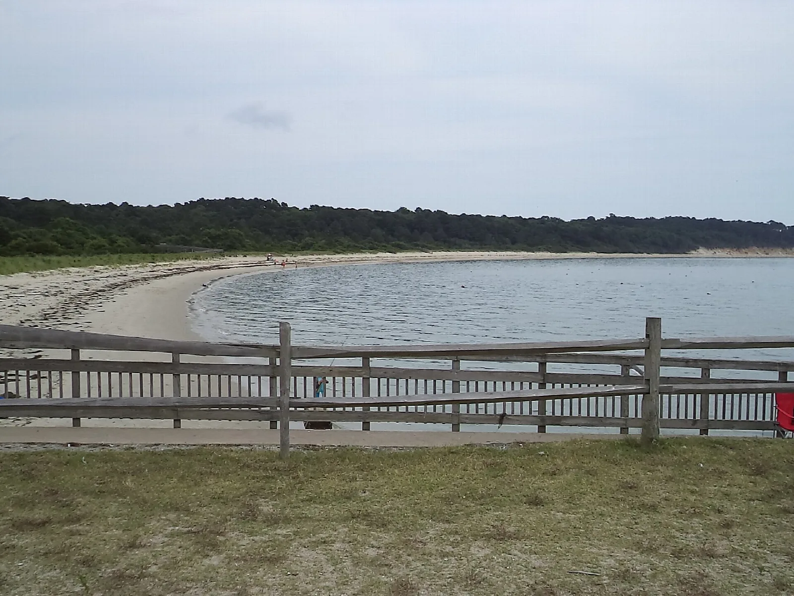 Curved sandy bay beach behind a wooden railing under a pale sky