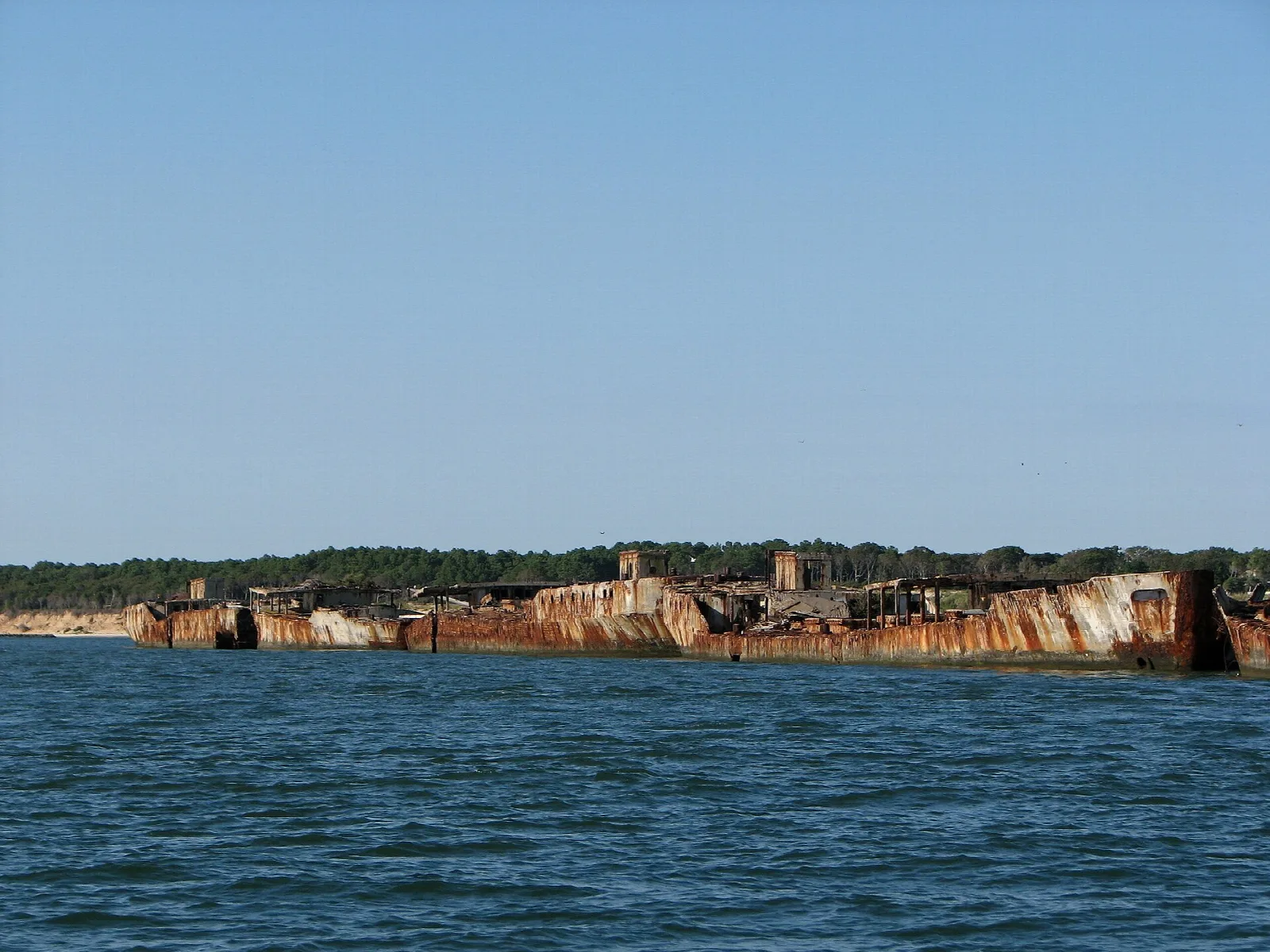Rusted concrete ship hulls forming a breakwater on open water