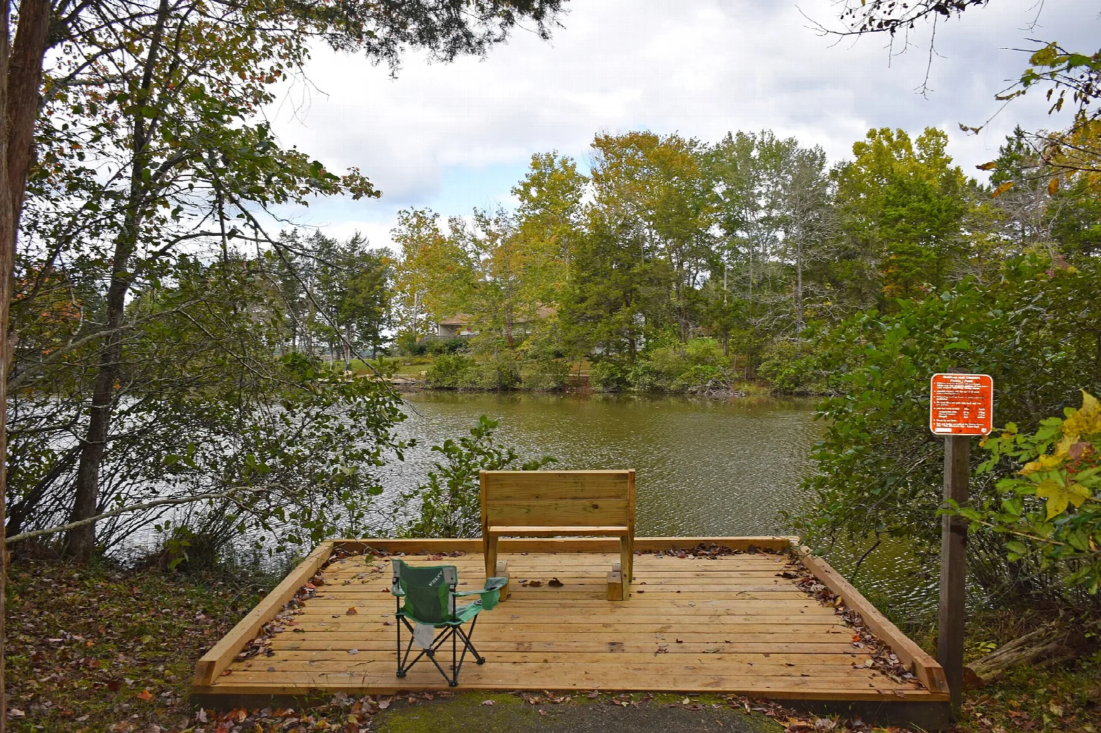 Wooden lakeside deck with a bench and a folding chair among trees
