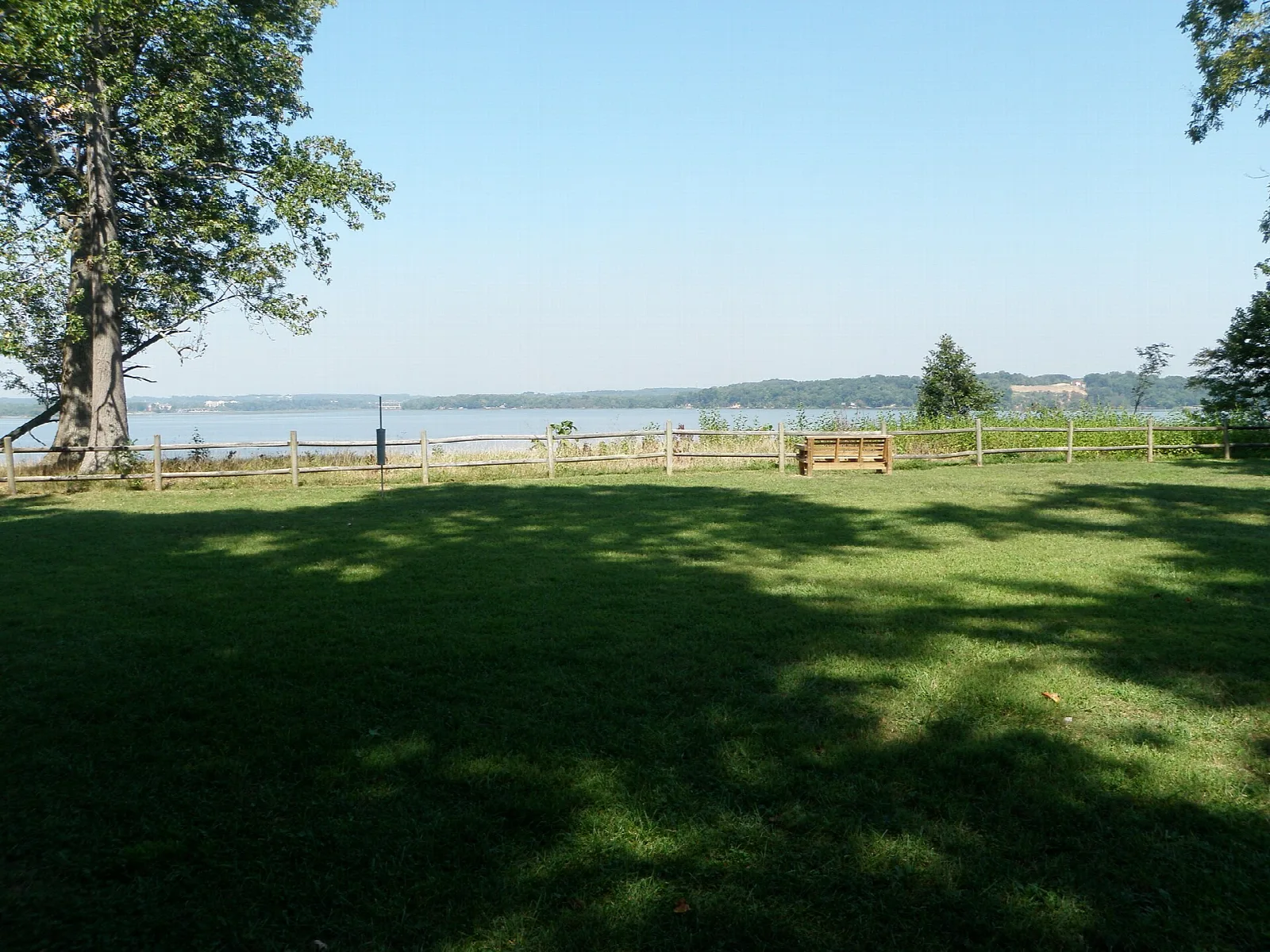 Lawn in shade with a rail fence and bay beyond under a clear sky