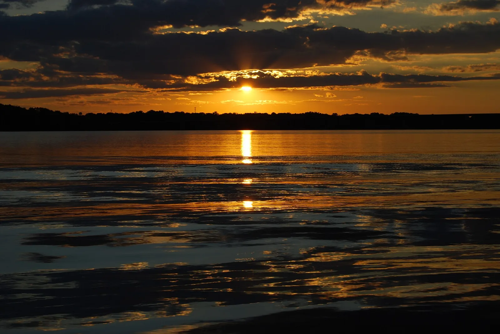 Sun setting over a wide lake with dark clouds and reflections