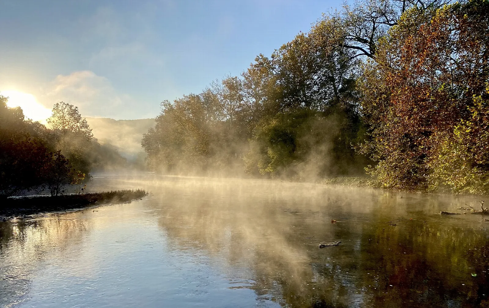Mist rising off a quiet river lined with autumn trees at sunrise