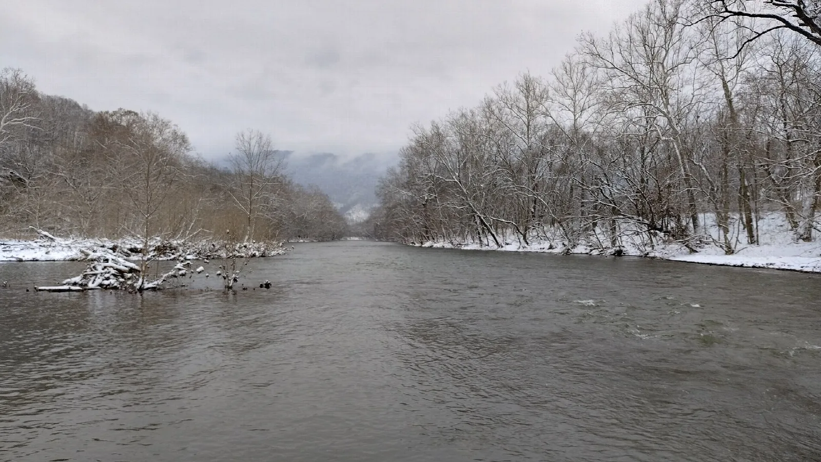 Wide gray river between snowy banks and bare trees