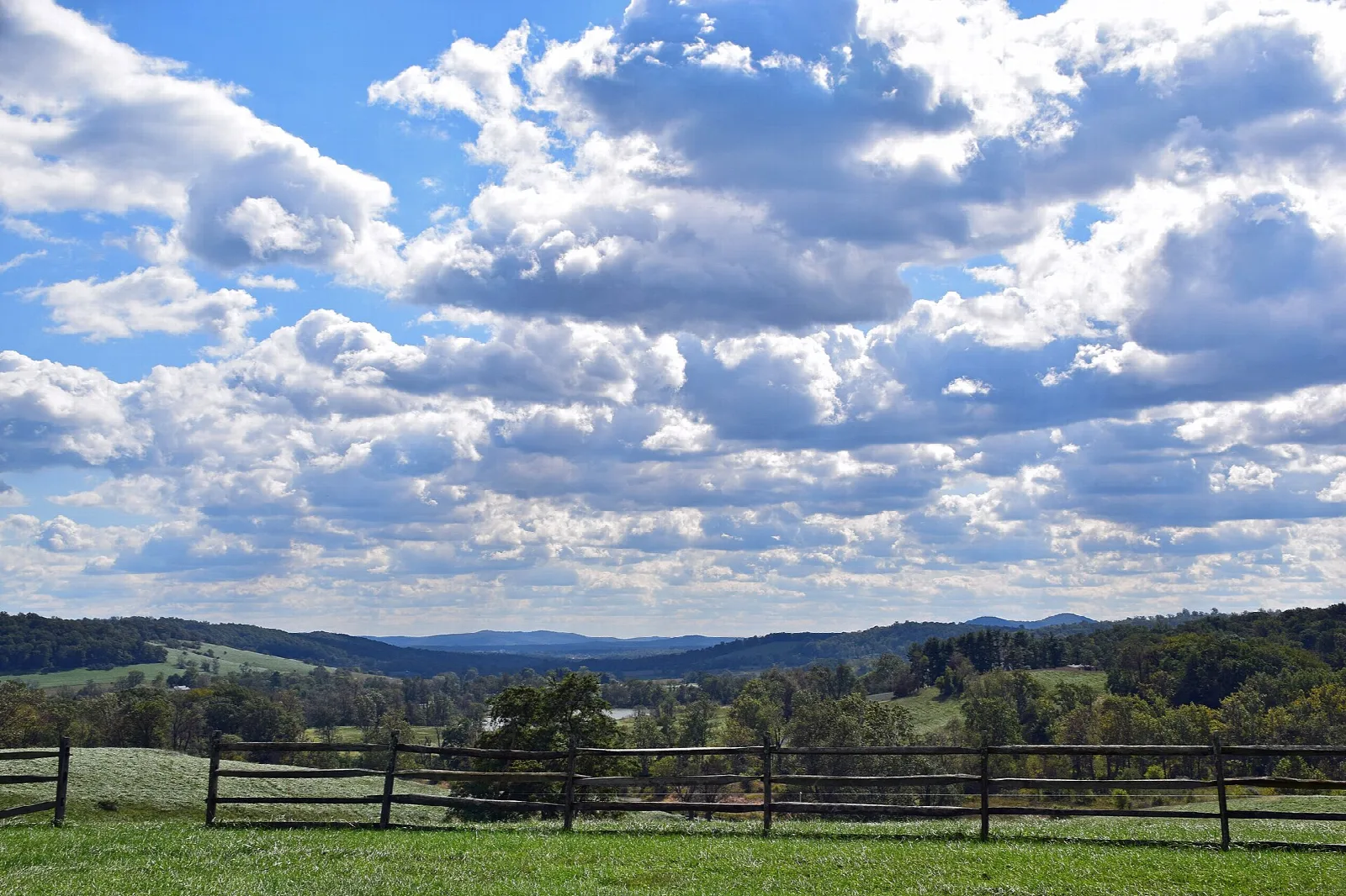 Green pasture with a wooden fence, distant ridges and big clouds