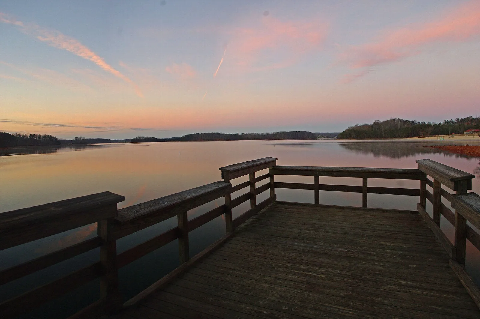 Wooden pier railing over still lake water at pink sunset
