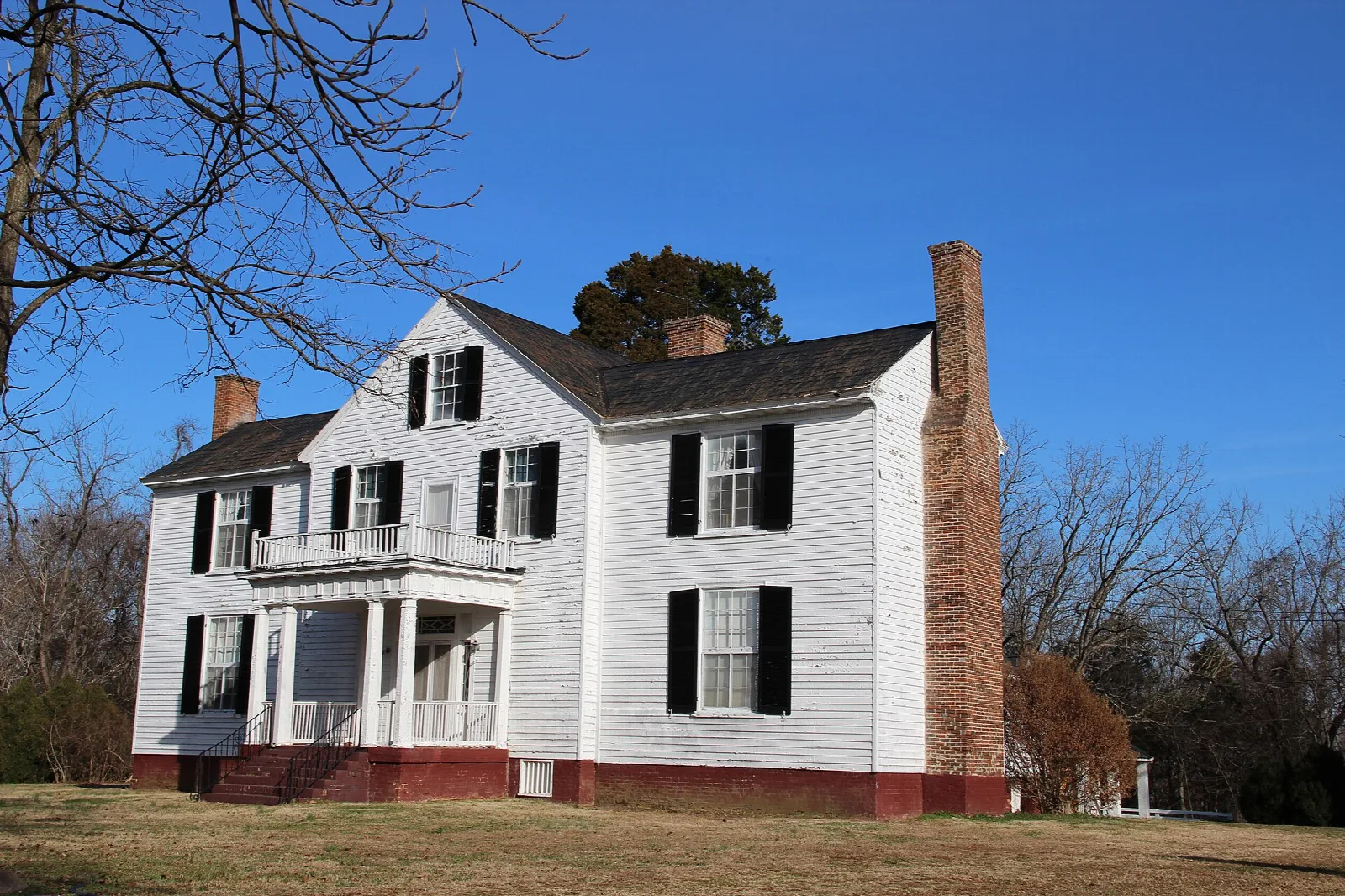 White two-story house with a brick chimney and porch against blue sky