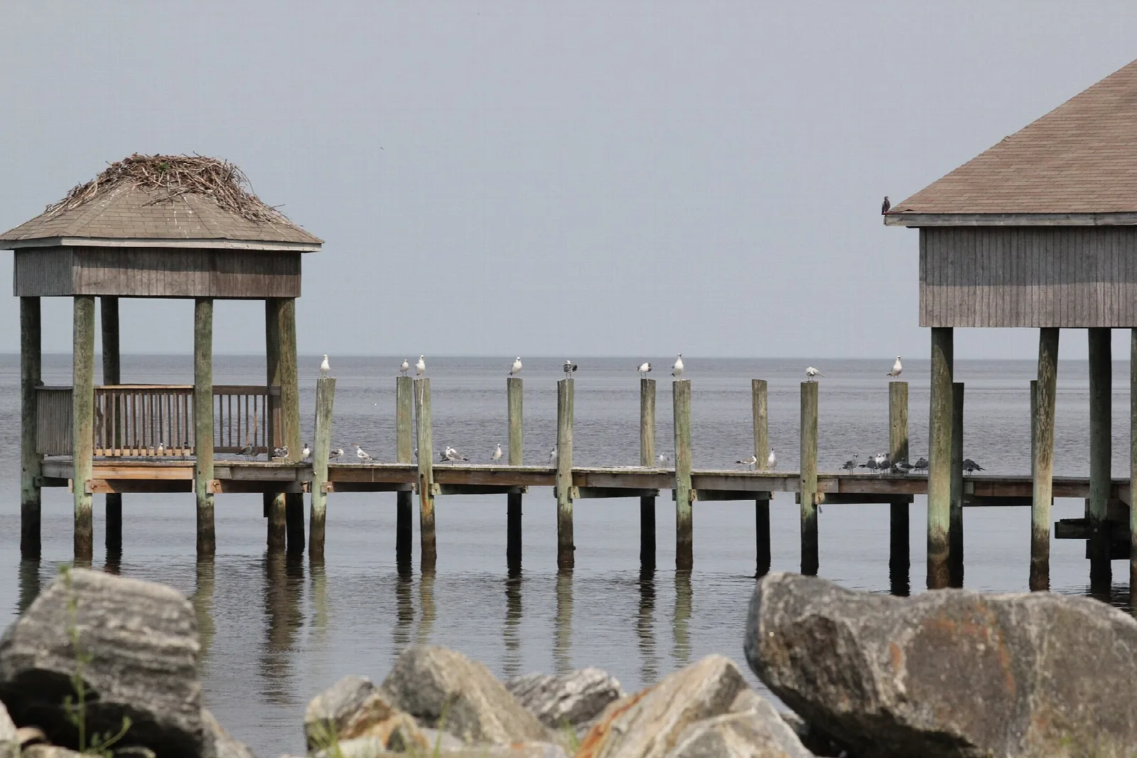 Wooden pier with two roofed shelters over calm gray water