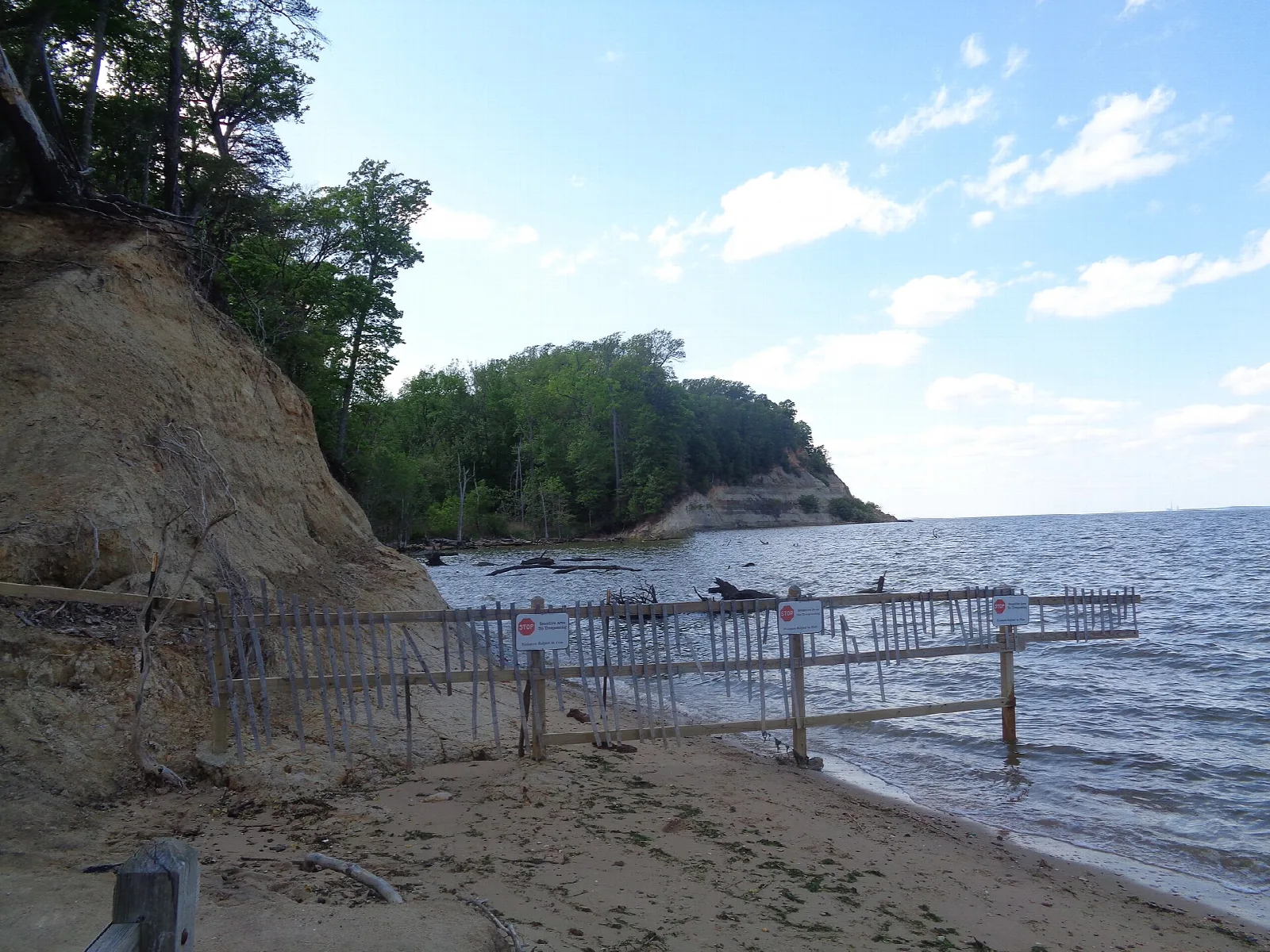 Eroded sandy cliff and beach beside a wide river with a fence