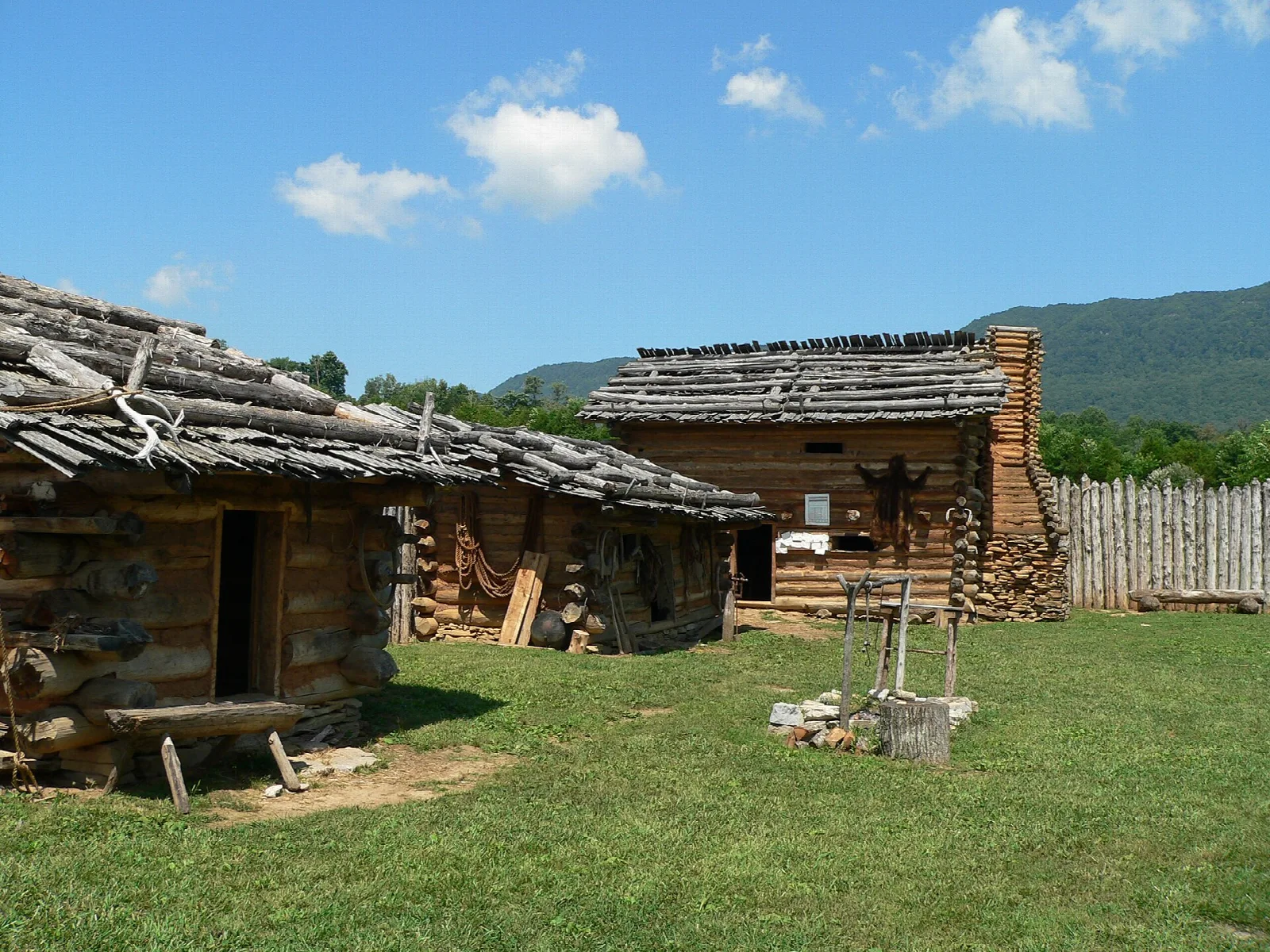 Weathered log cabins and a stockade fence on a grassy lawn