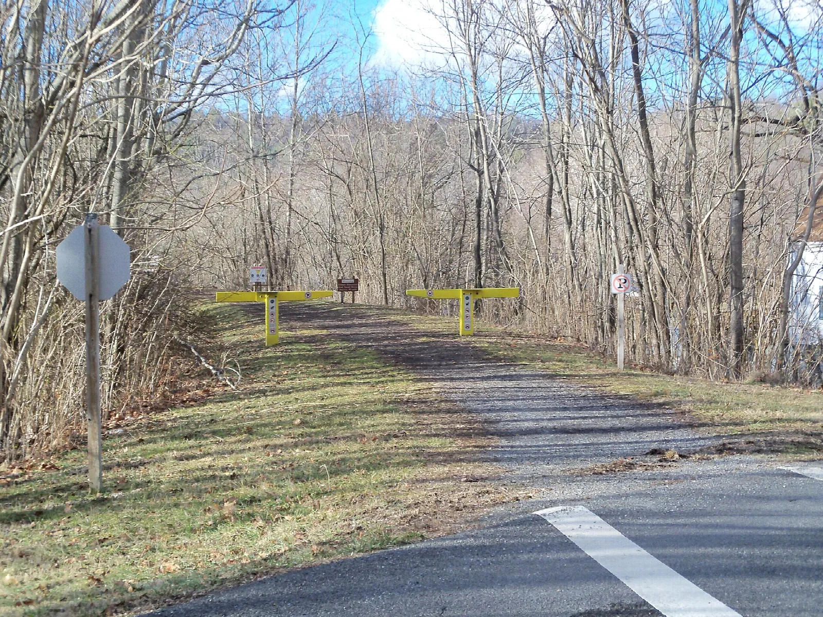 Paved and gravel trail crossing a road, lined with bare trees