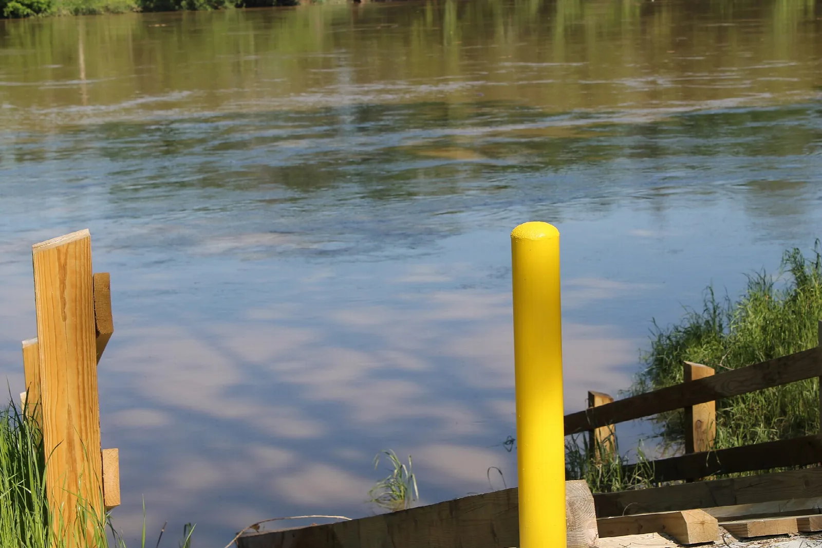 Wooden rails and a yellow post beside river water at a launch