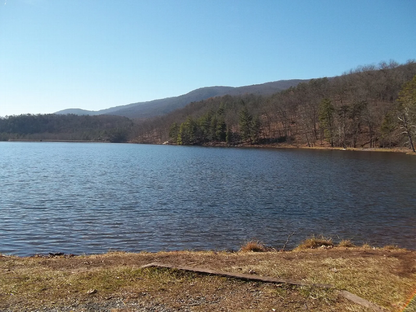 Wide lake with forested hills beyond a rocky shore
