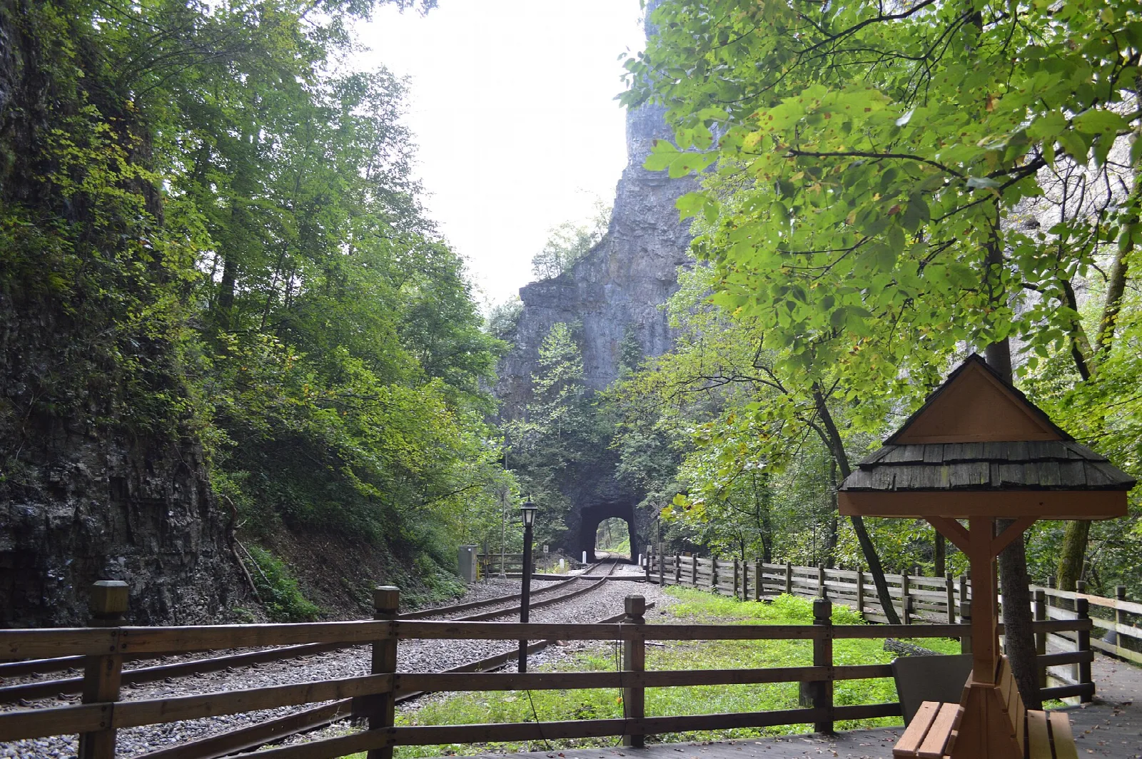 Railroad track and wooden gazebo leading toward a tunnel in a rock wall