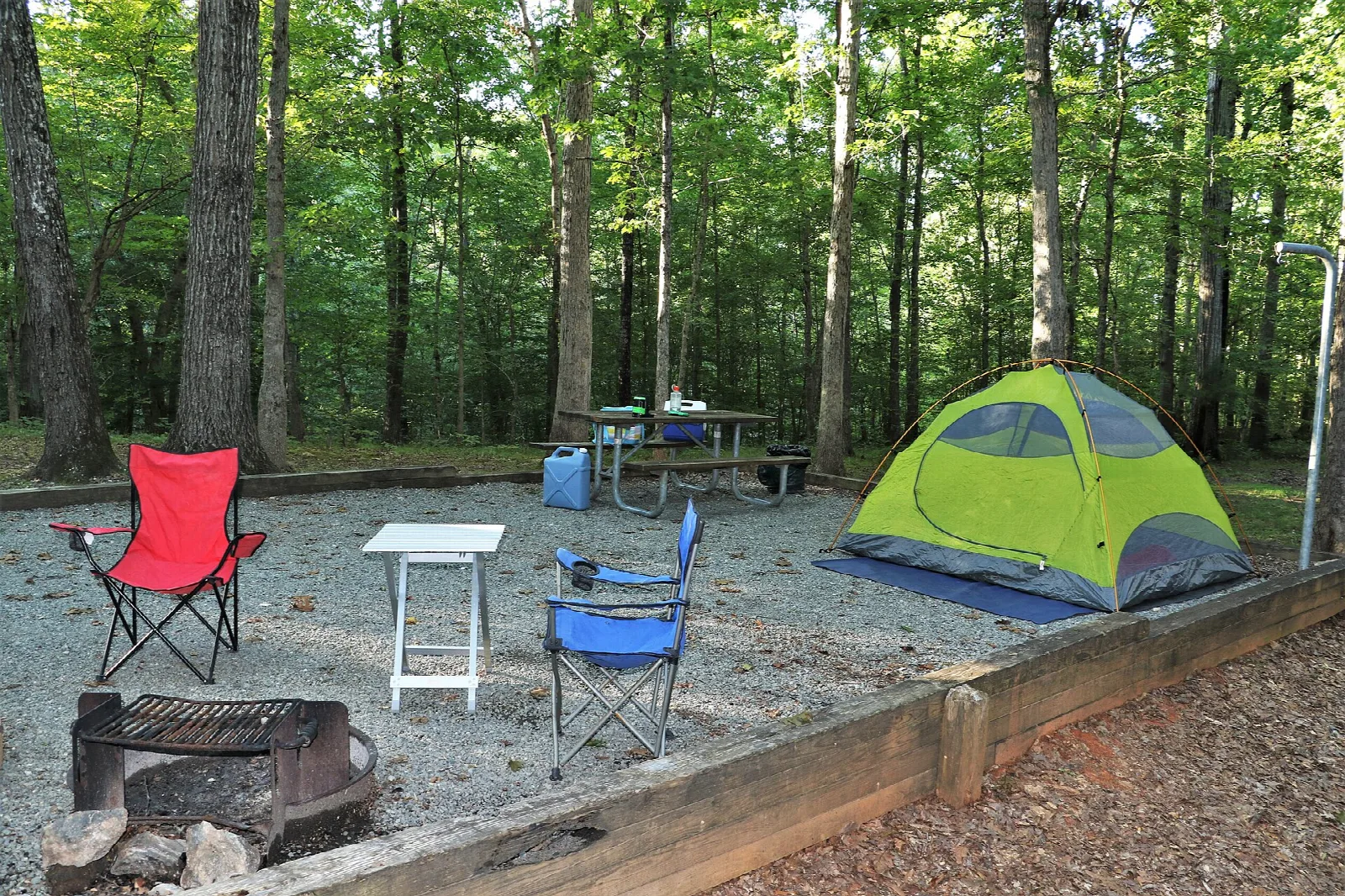 Tent, camp chairs and fire ring at a wooded campsite