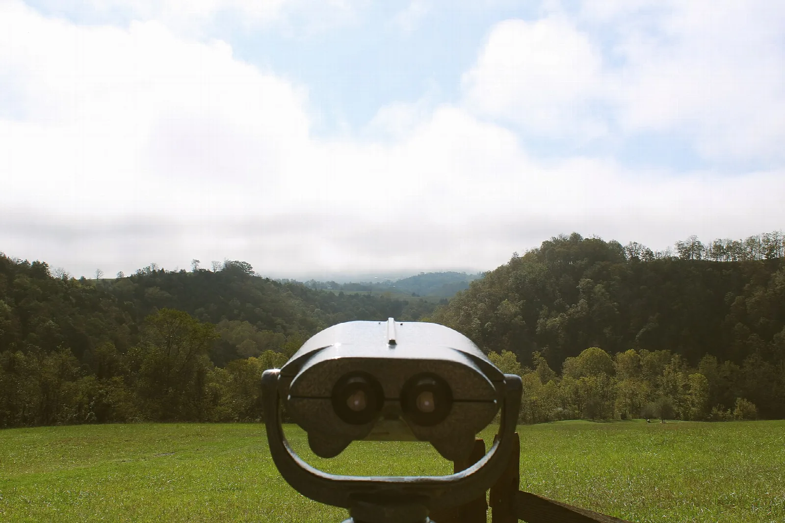 Coin-operated viewfinder in a meadow facing forested hills
