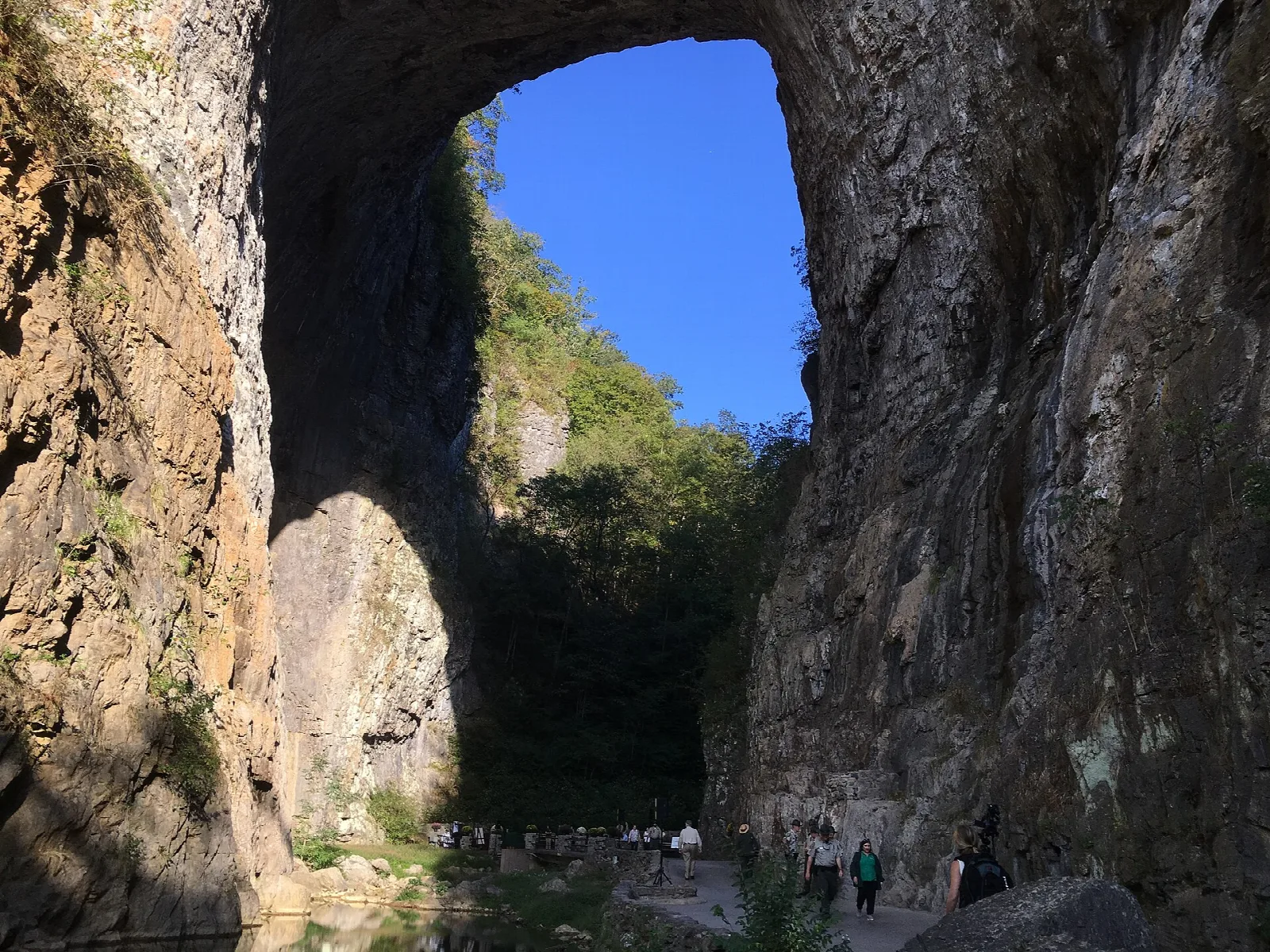 Tall rock arch with a bright opening and a few visitors below