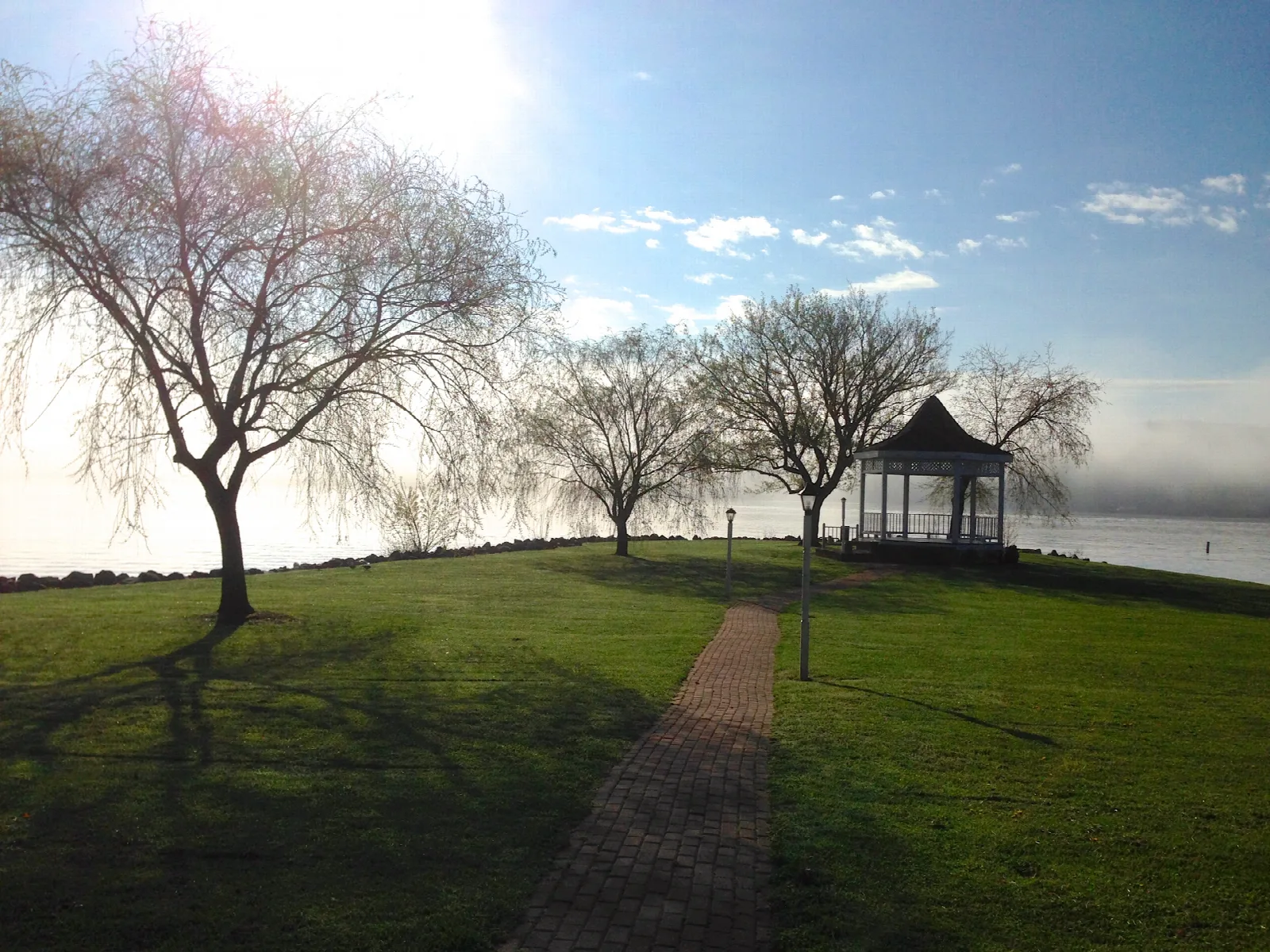 Lawn with a gazebo and bare trees beside the lake at sunrise