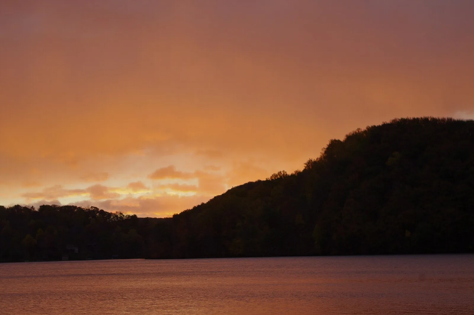 Calm reservoir with dark hills under an orange dawn sky