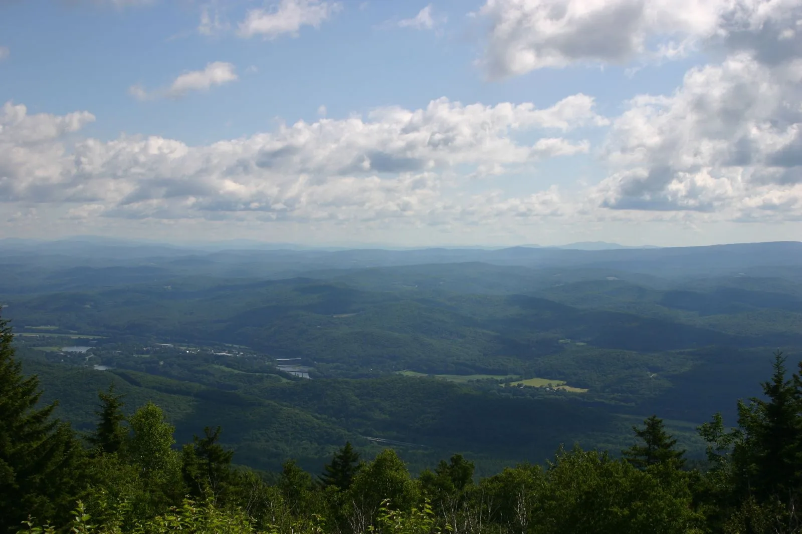 Forested valley and distant hills under scattered clouds, seen from a high point