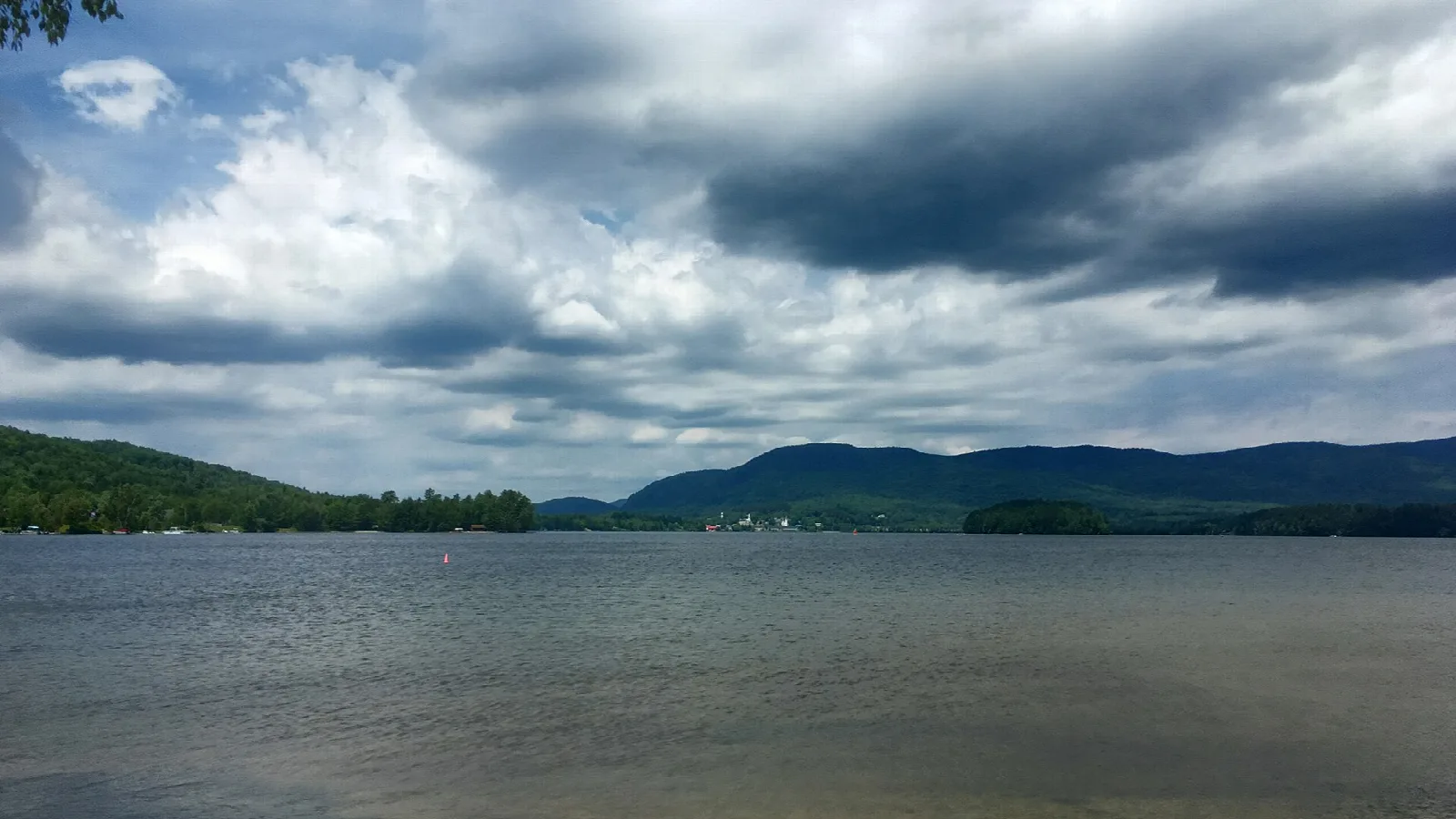 Wide lake under heavy clouds with low hills along the far shore