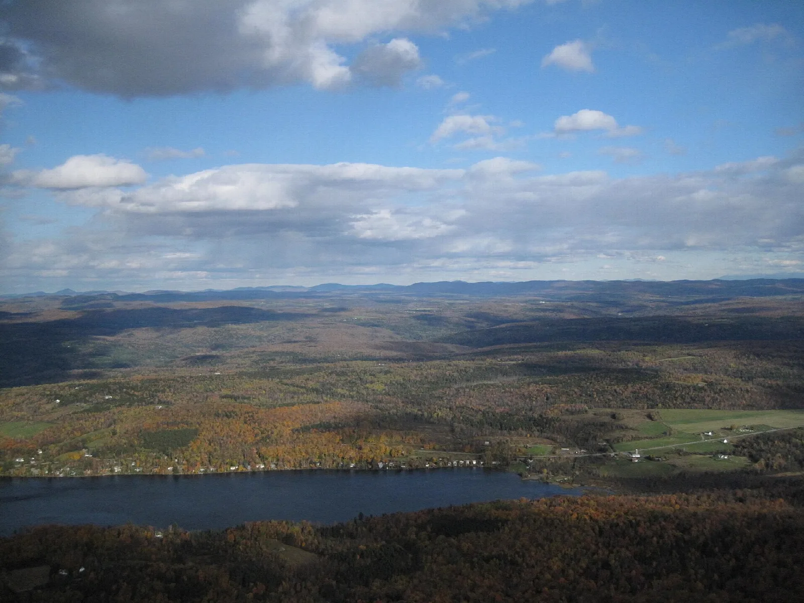 Wide view over farmland and a lake under a blue sky with clouds