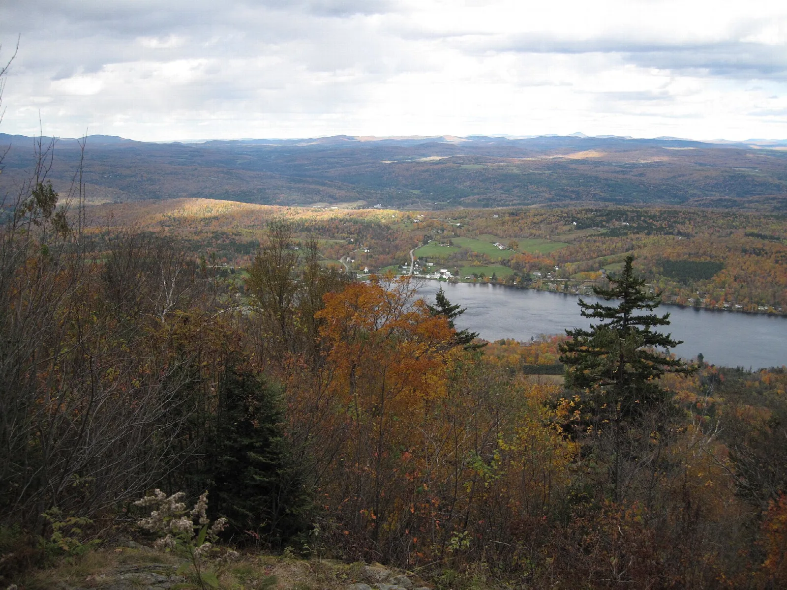 View over autumn trees to a lake and hazy hills from near a summit