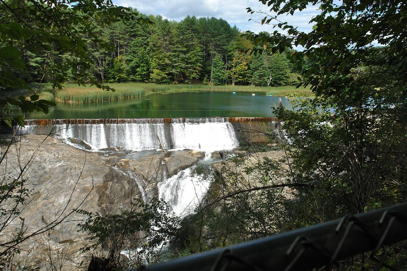 Small waterfall and dam with a calm pond above, ringed by trees