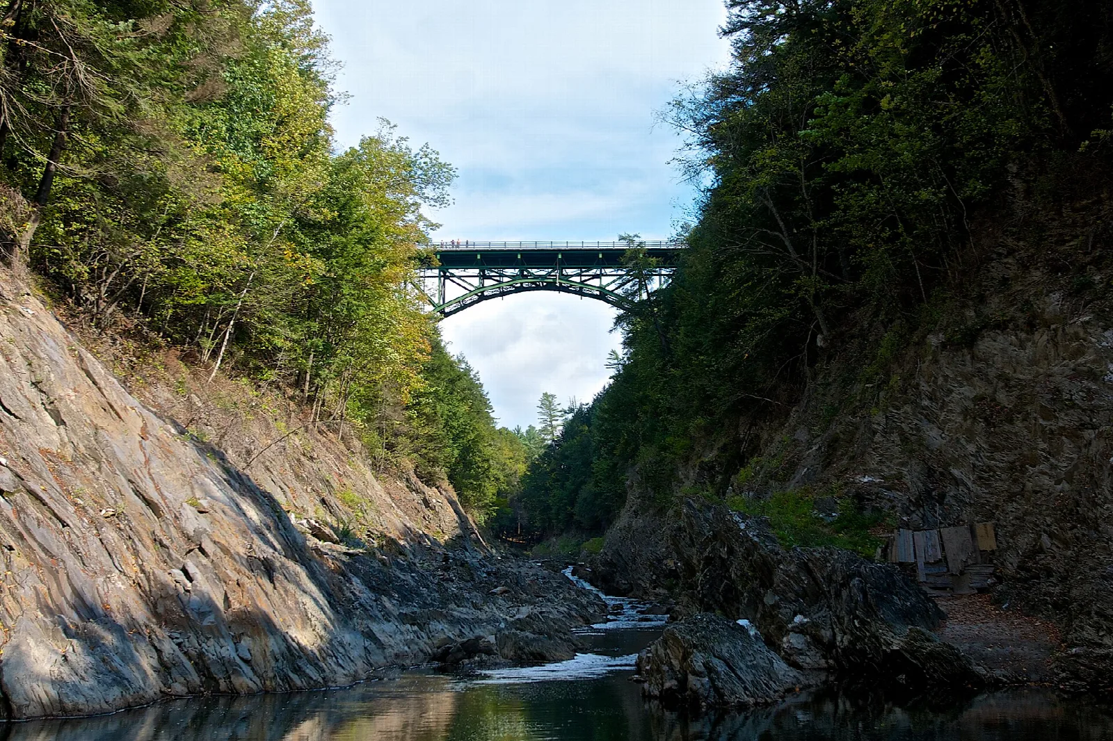 Steel bridge spanning a rocky gorge with trees on both sides