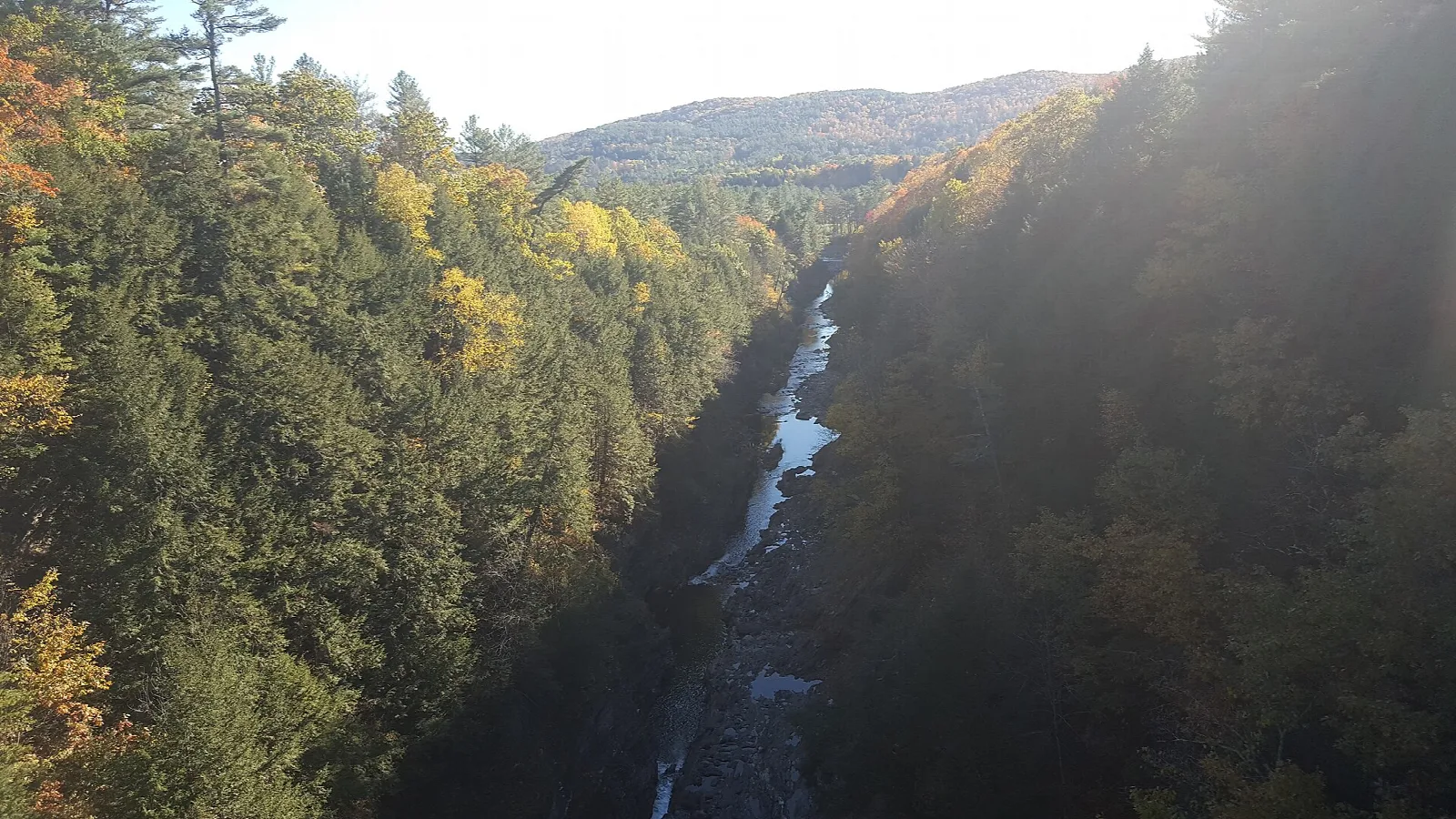 Forested gorge with a narrow river far below under autumn hills