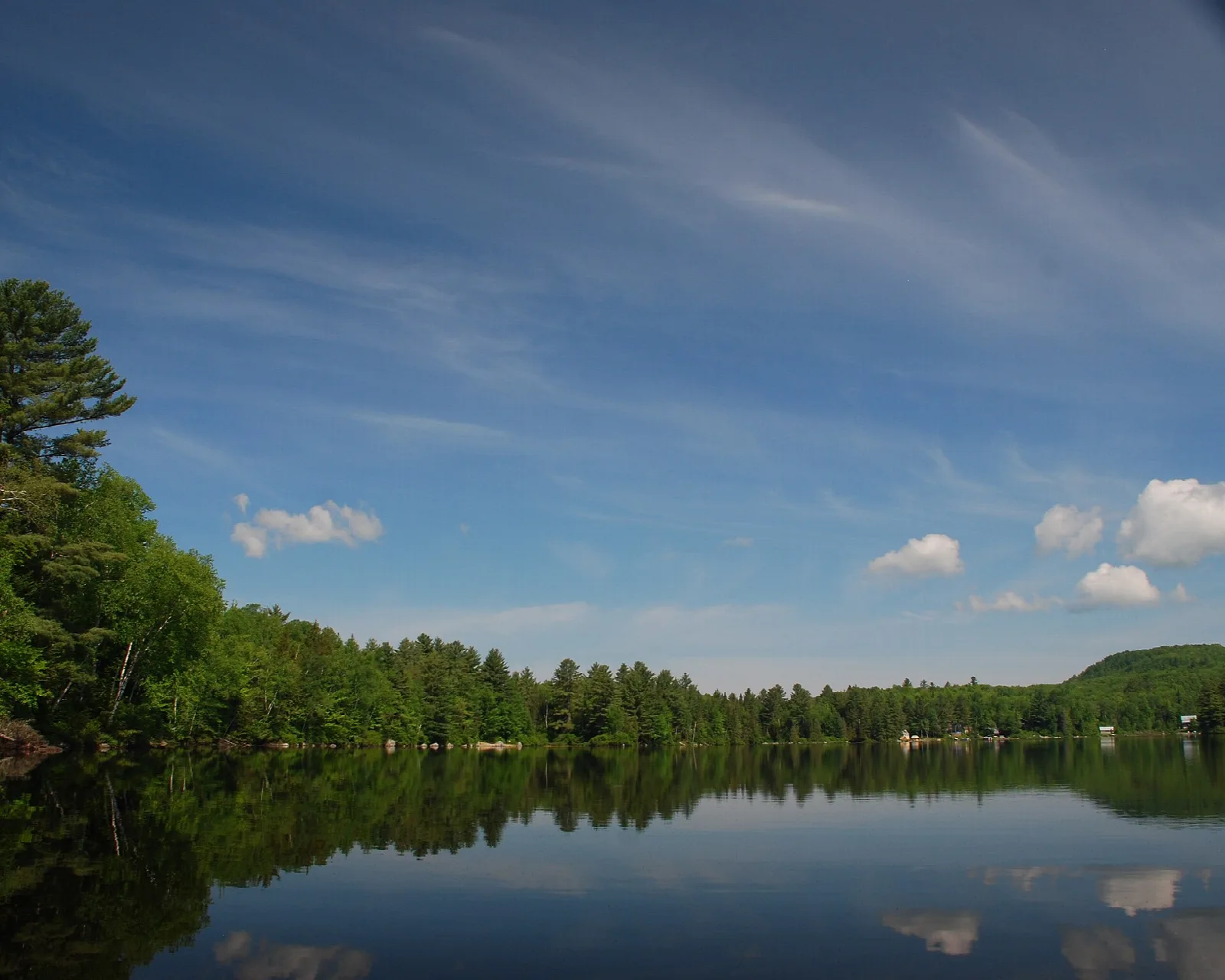 Calm pond reflecting trees and blue sky with a low hill beyond