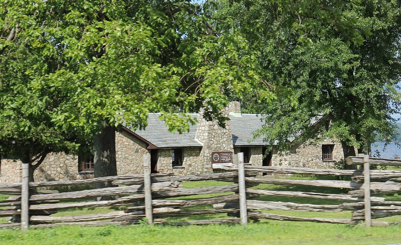 Stone CCC building behind a split-rail fence and trees