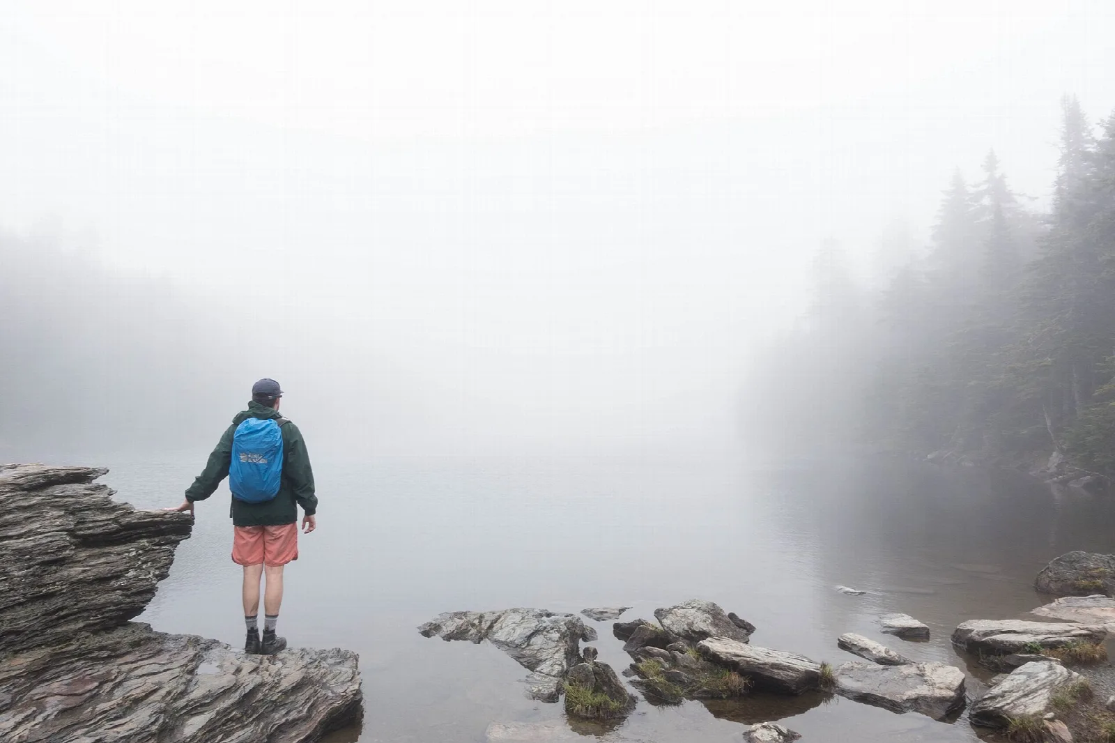 Hiker standing on rocks at the edge of a misty pond