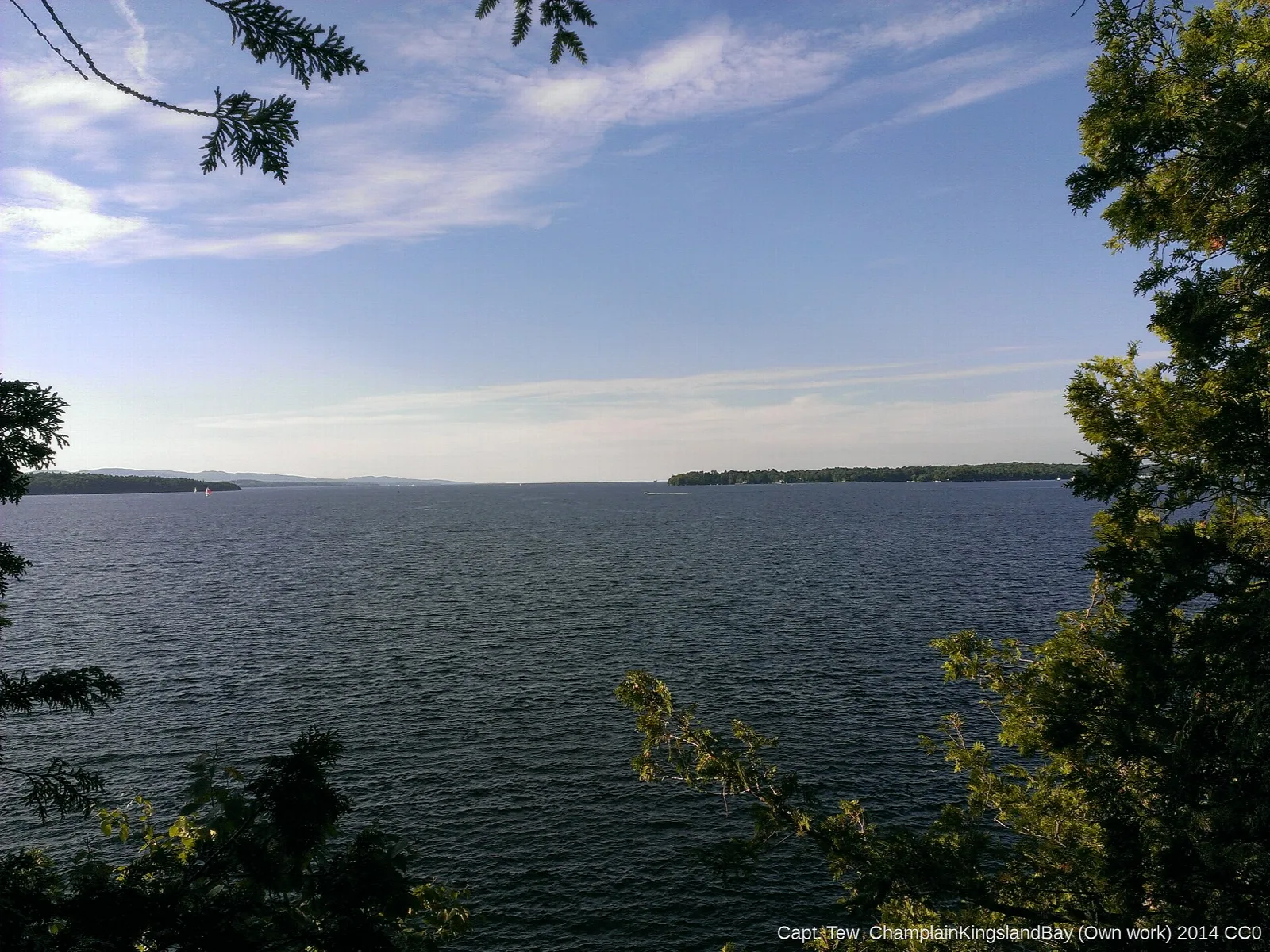 Wide view of Lake Champlain framed by trees on a sunny day