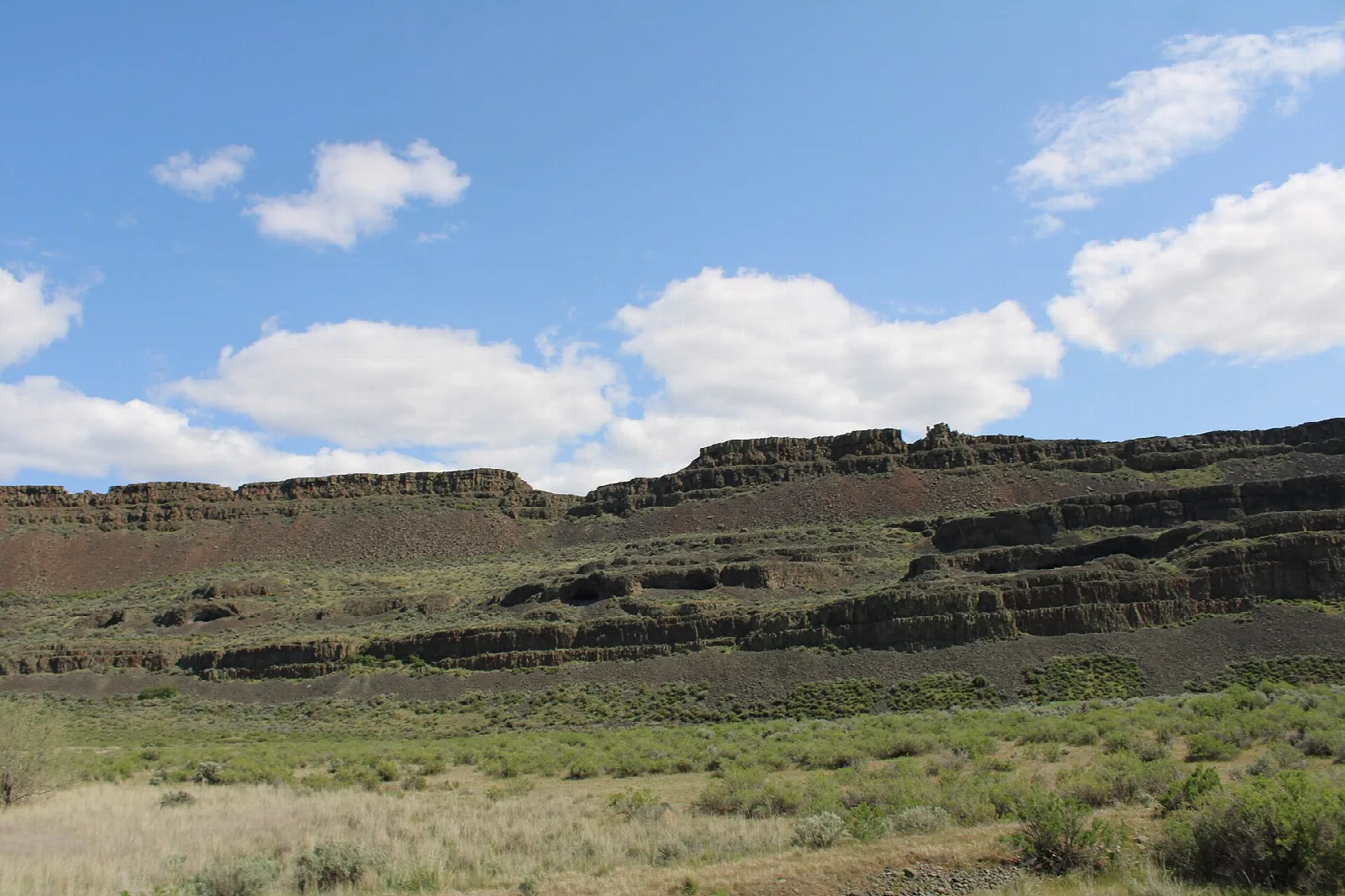 Layered basalt cliff above sagebrush with a gravel road below