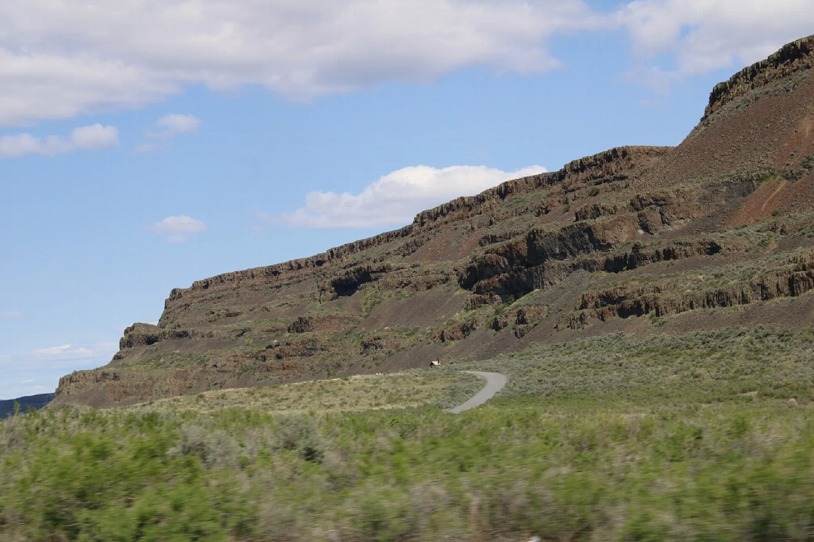 Dark basalt cliff band above sagebrush flats and a paved road