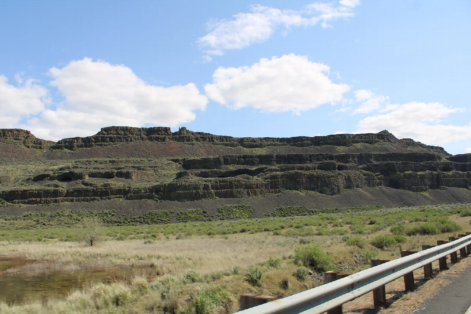 Long basalt cliff over grass and a guardrail beside the road