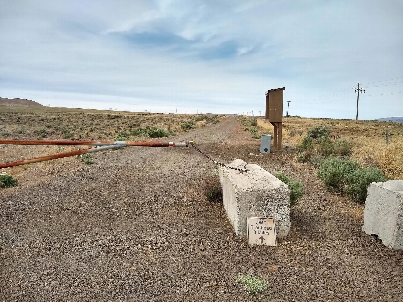 Gravel trail with a gate and sign across open dry country