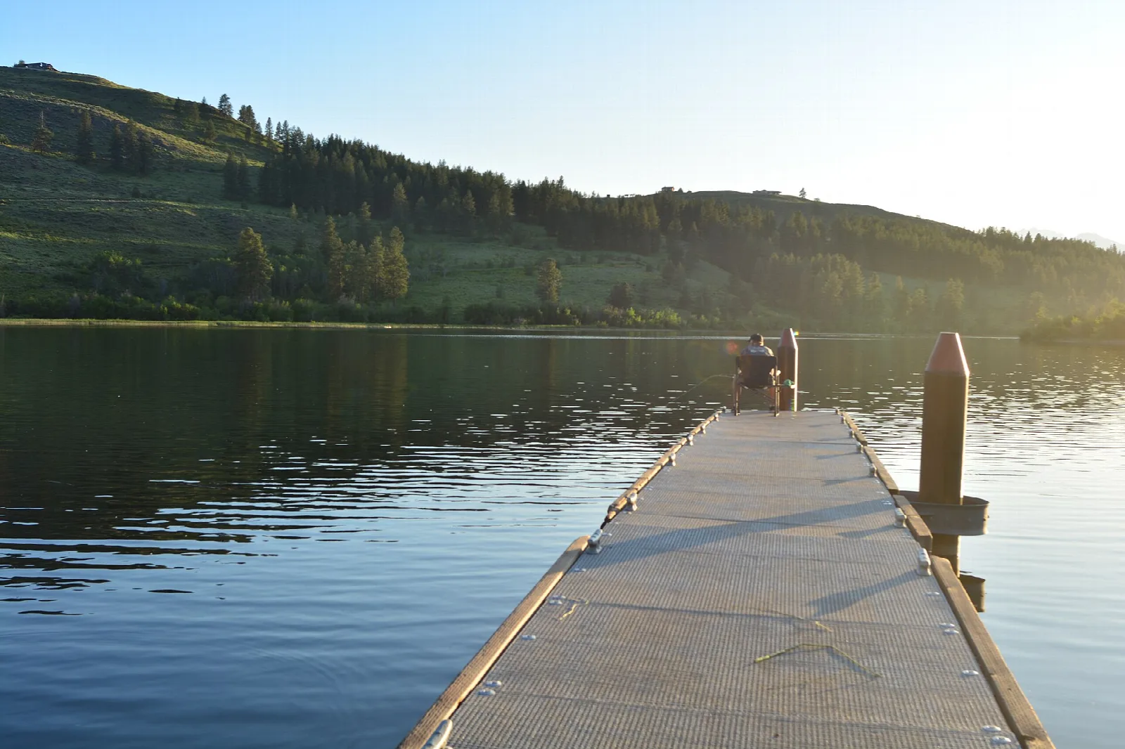 Floating pier extending over a still lake with hills beyond
