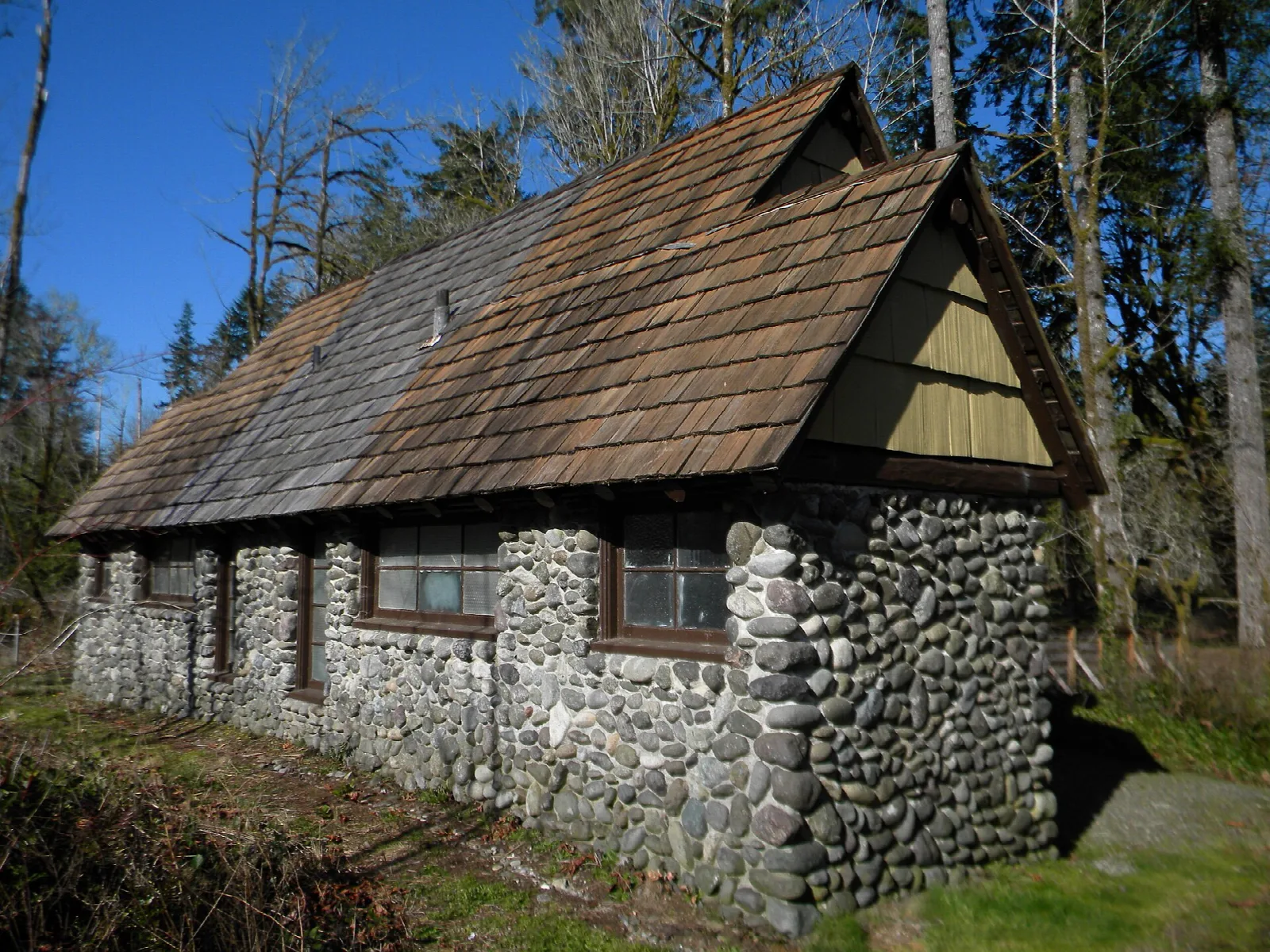 Stone-walled building with a shingled roof among trees